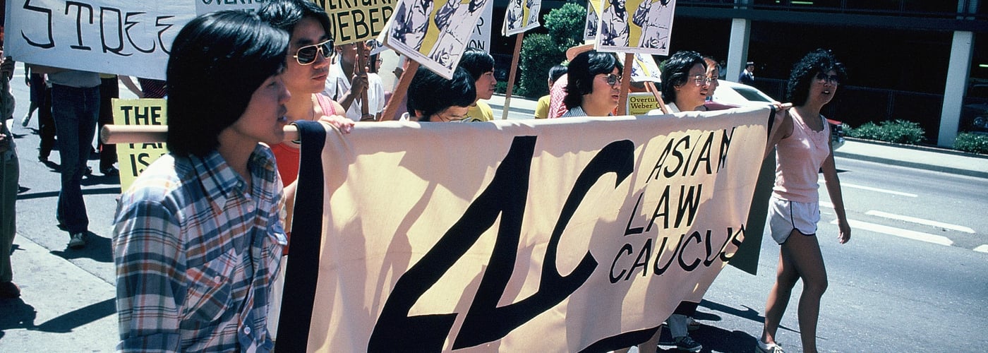 Row of men hold banner reading "ALC Asian Law Caucus" in front of marchers holding other signs