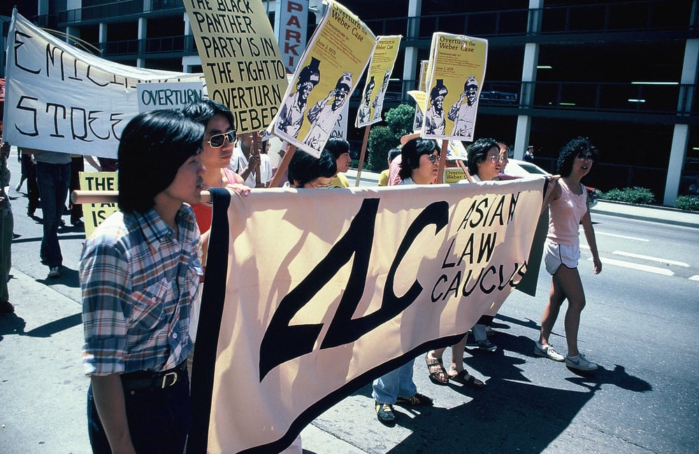 Asian Law Caucus and Asian Law Alliance staff carrying an ALC banner at a protest against the Weber v. Kaiser Aluminum & Chemical decision in the 5th Circuit. Behind the group, there are many other people carrying signs and banners.