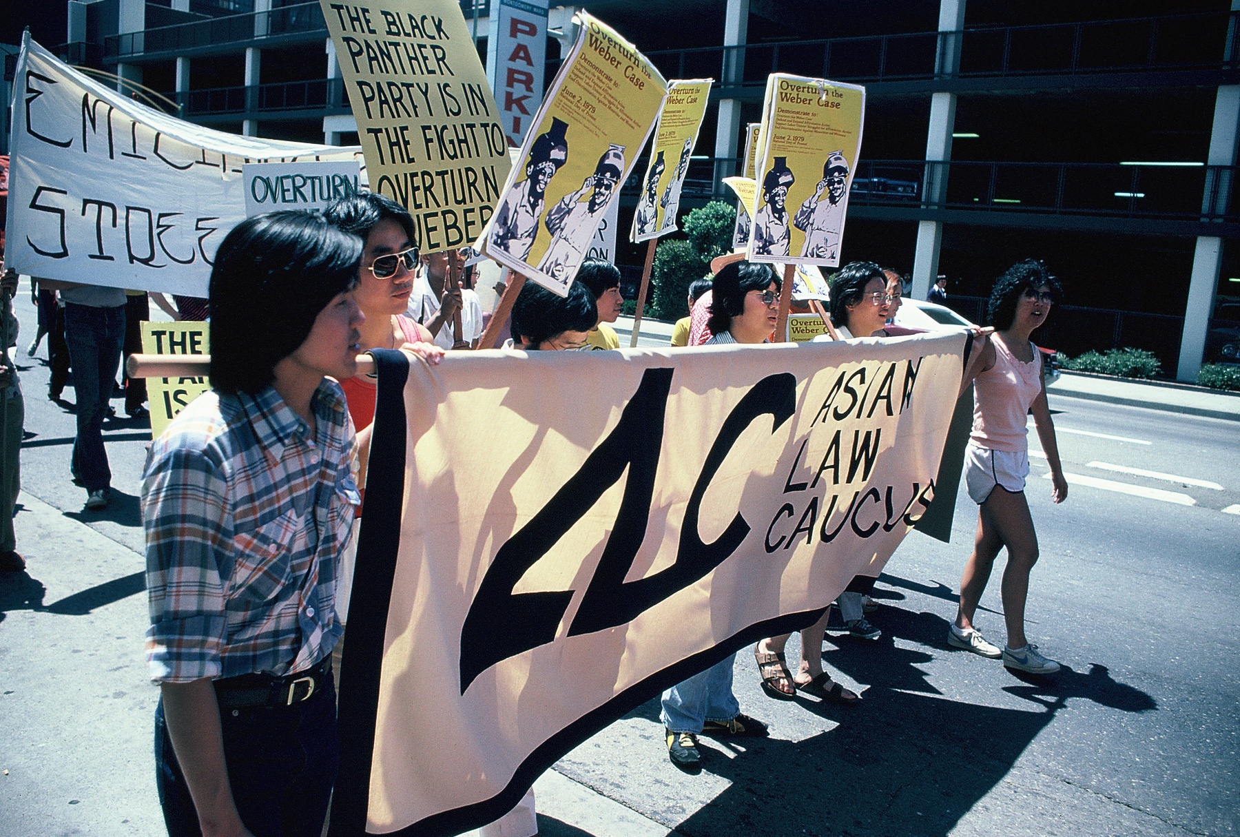 Asian Law Caucus and Asian Law Alliance staff carrying an ALC banner at a protest against the Weber v. Kaiser Aluminum & Chemical decision in the 5th Circuit. Behind the group, there are many other people carrying signs and banners.