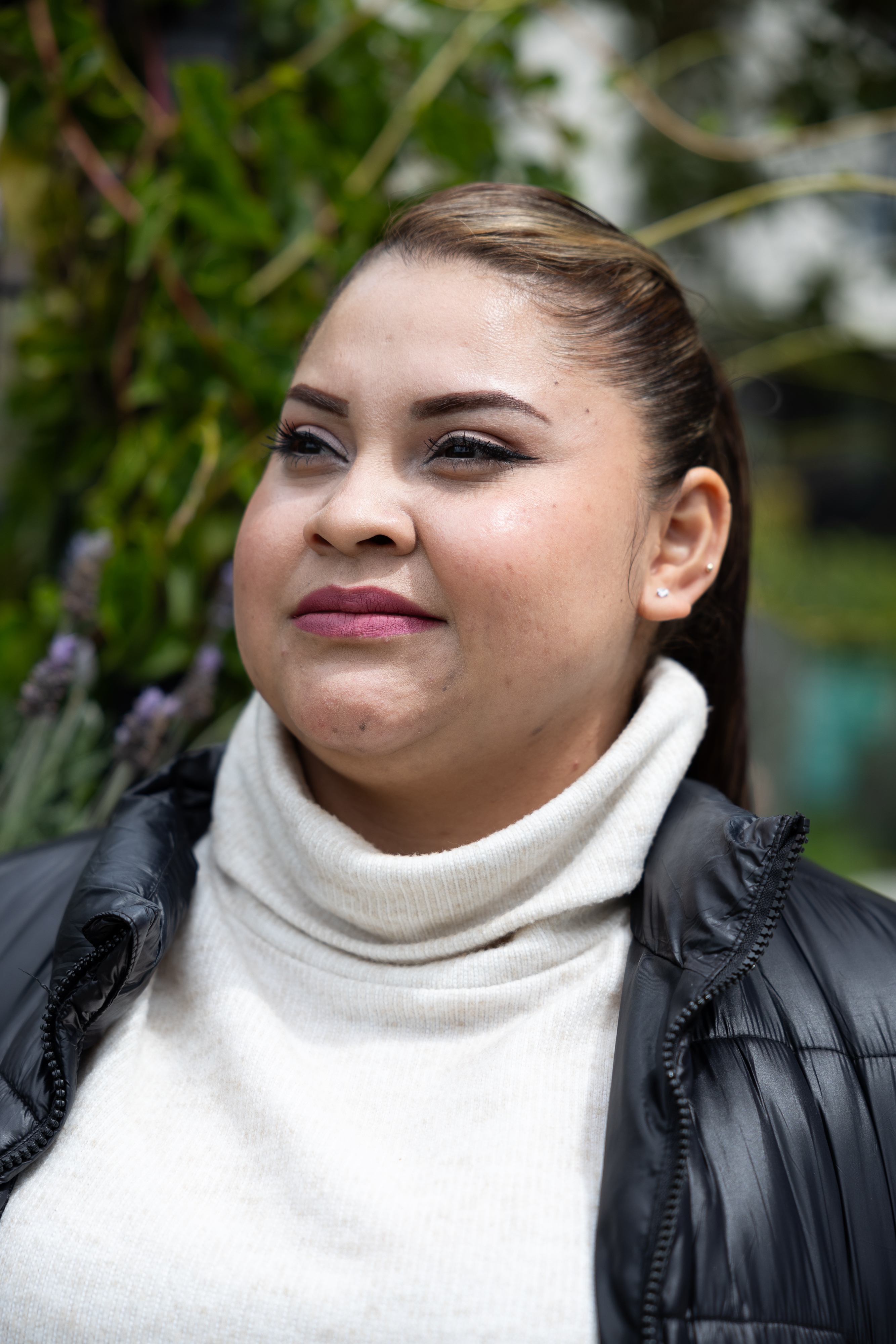 Photo: A woman wearing a turtleneck and puffy jacket stands outside and looks away from the camera.