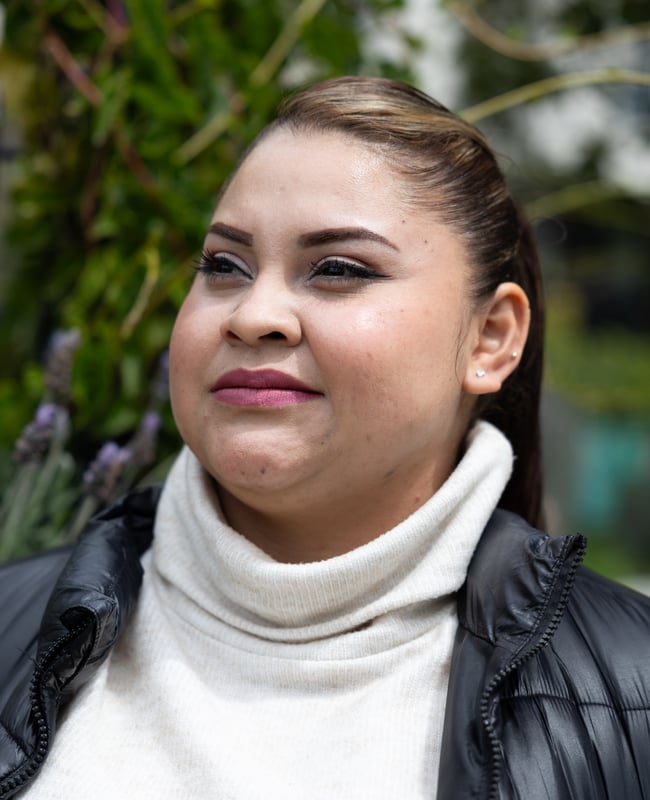 Photo: A woman wearing a turtleneck and puffy jacket stands outside and looks away from the camera.