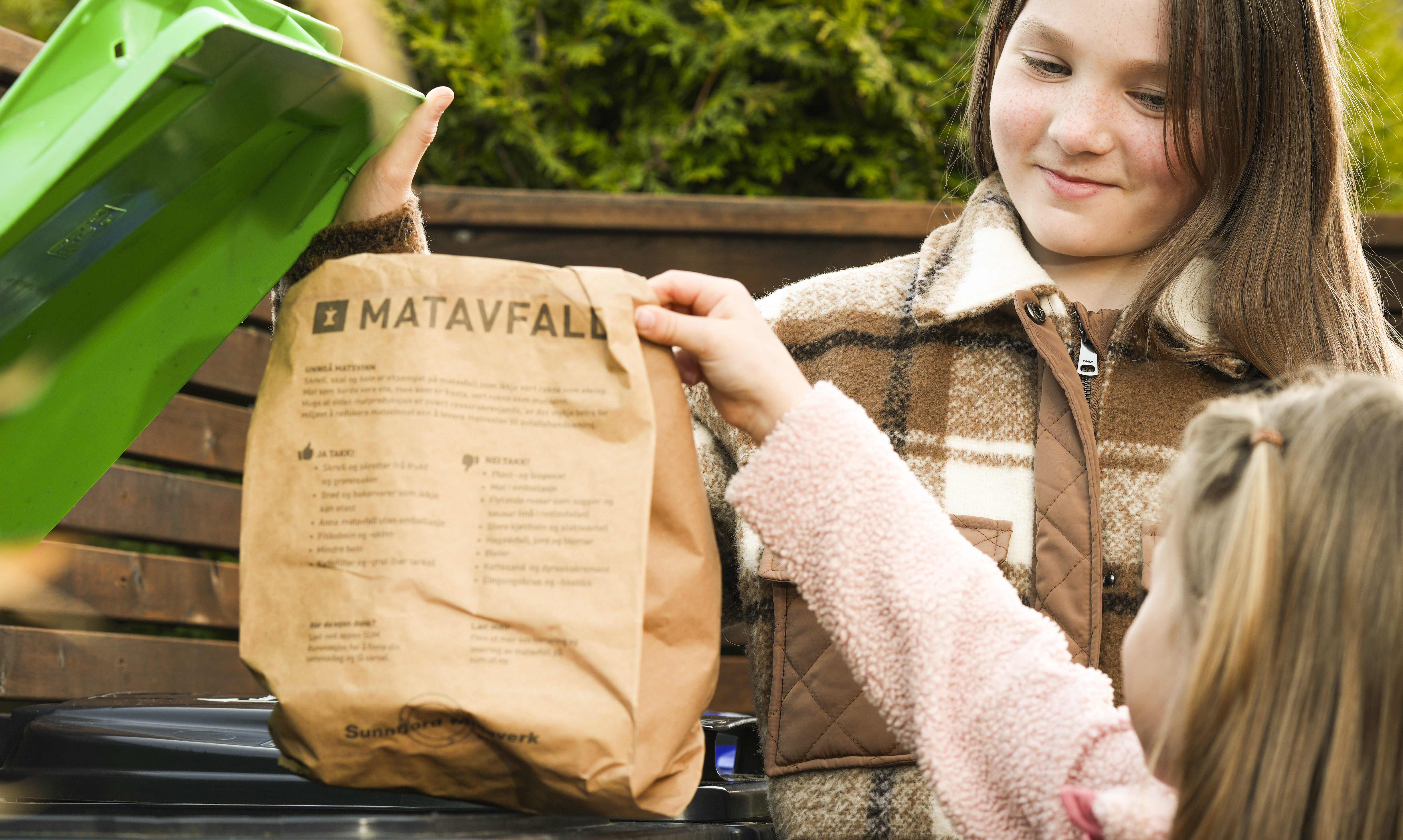 Bilde av to jenter som kaster ein pose med matavfall i dunken.