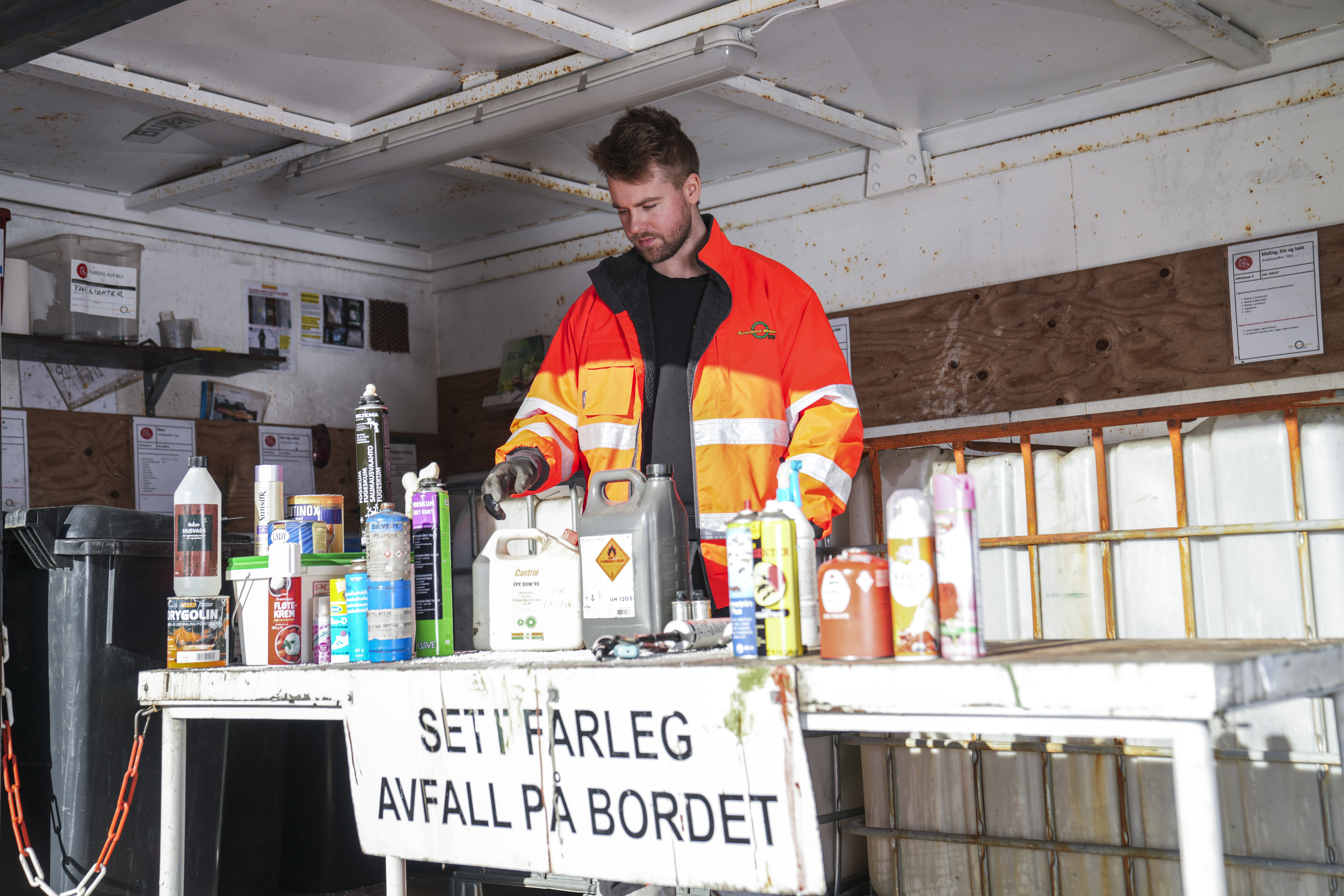 Bilde av gjenvinningsoperatør som rydder eit bord med farleg avfall, som til dømes sprayboksar og Kremtopp.
