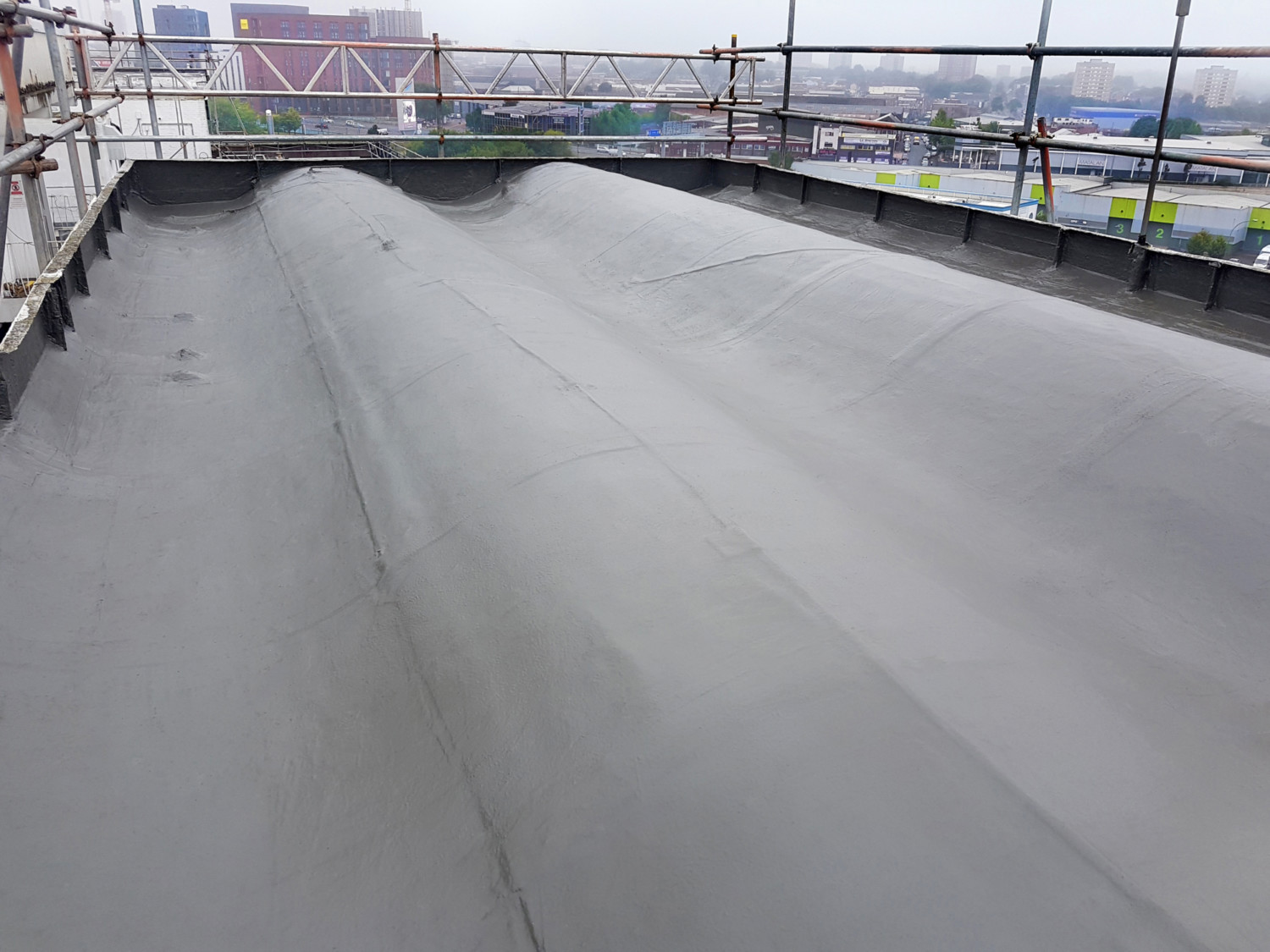 Grey concrete rooftop with metal scaffolding barriers around perimeter, construction site visible in background under overcast sky.
