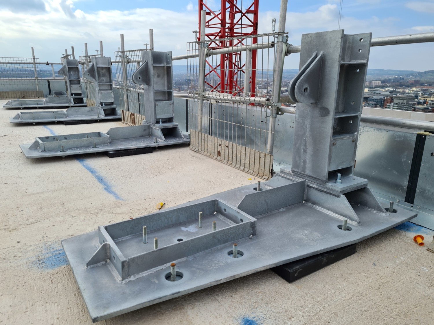 Grey concrete construction components on building site with red crane in background, cloudy sky visible.