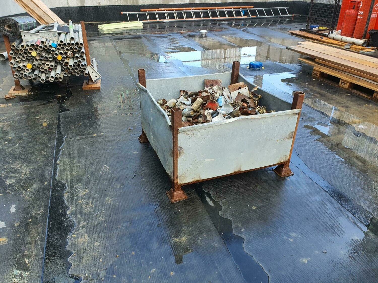 Metal collection bins on wet concrete floor in industrial warehouse with ladders and wooden pallets in background.