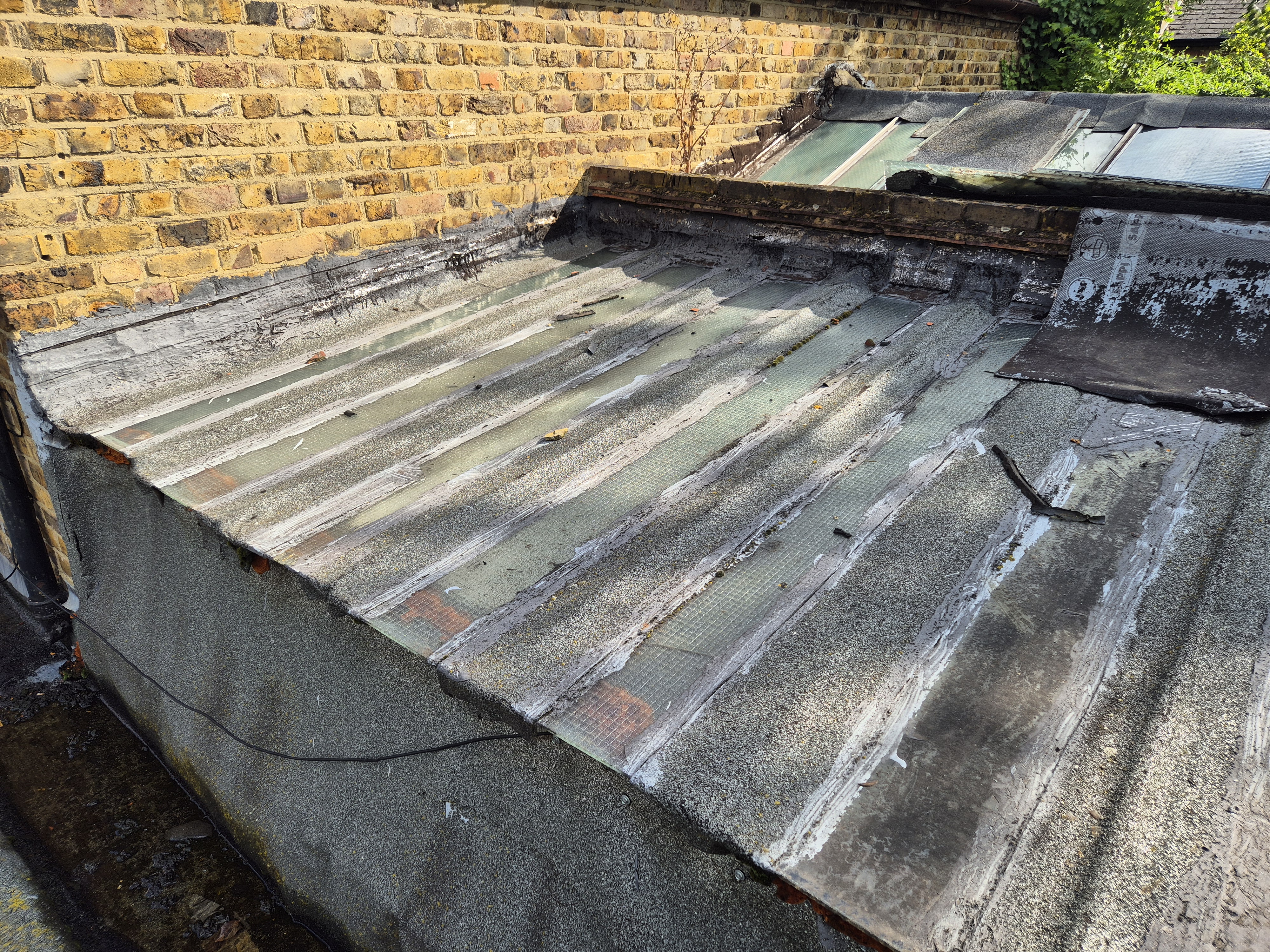 Weathered flat roof with corrugated metal sheets and brick wall. Green moss patches visible on grey deteriorating surface.