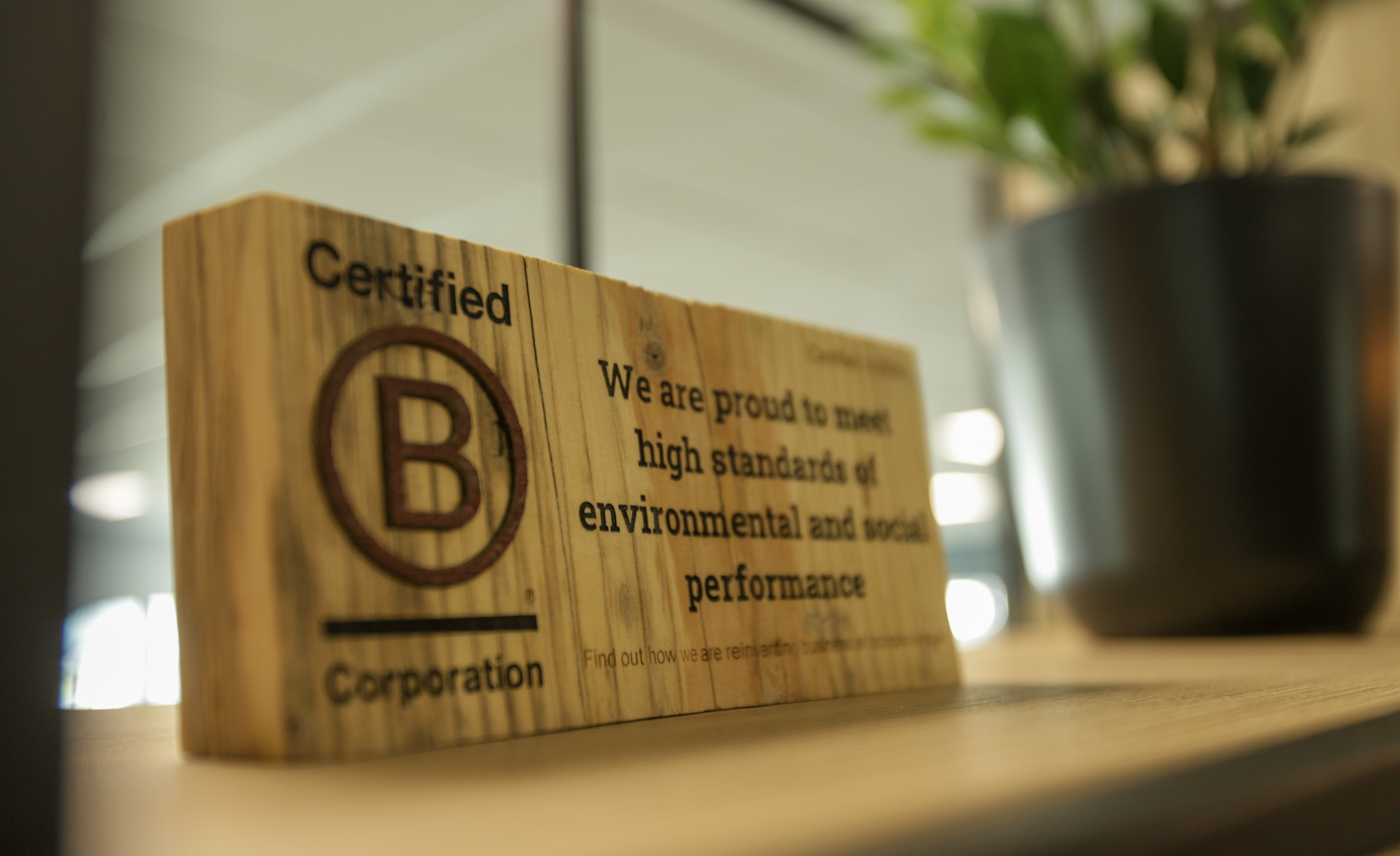 Wooden B Corporation certification plaque on desk with text about environmental and social performance standards.