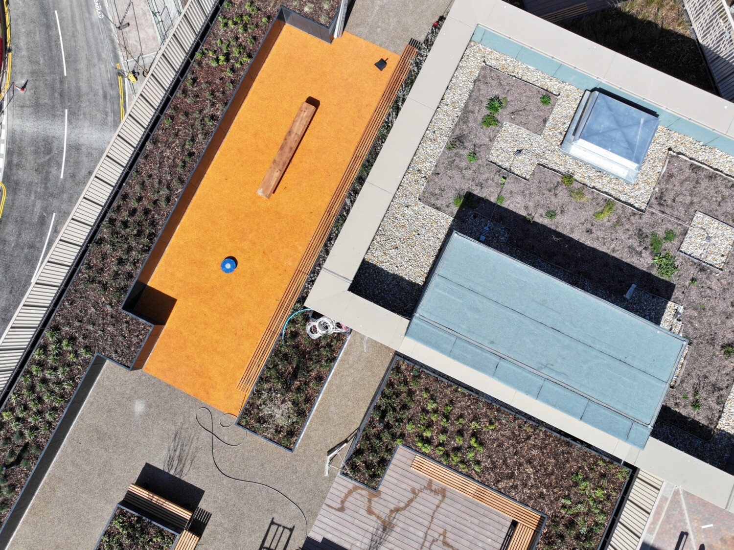 Aerial view of modern buildings with orange and beige rooftops, blue swimming pool, grey concrete surfaces, and landscaped areas.