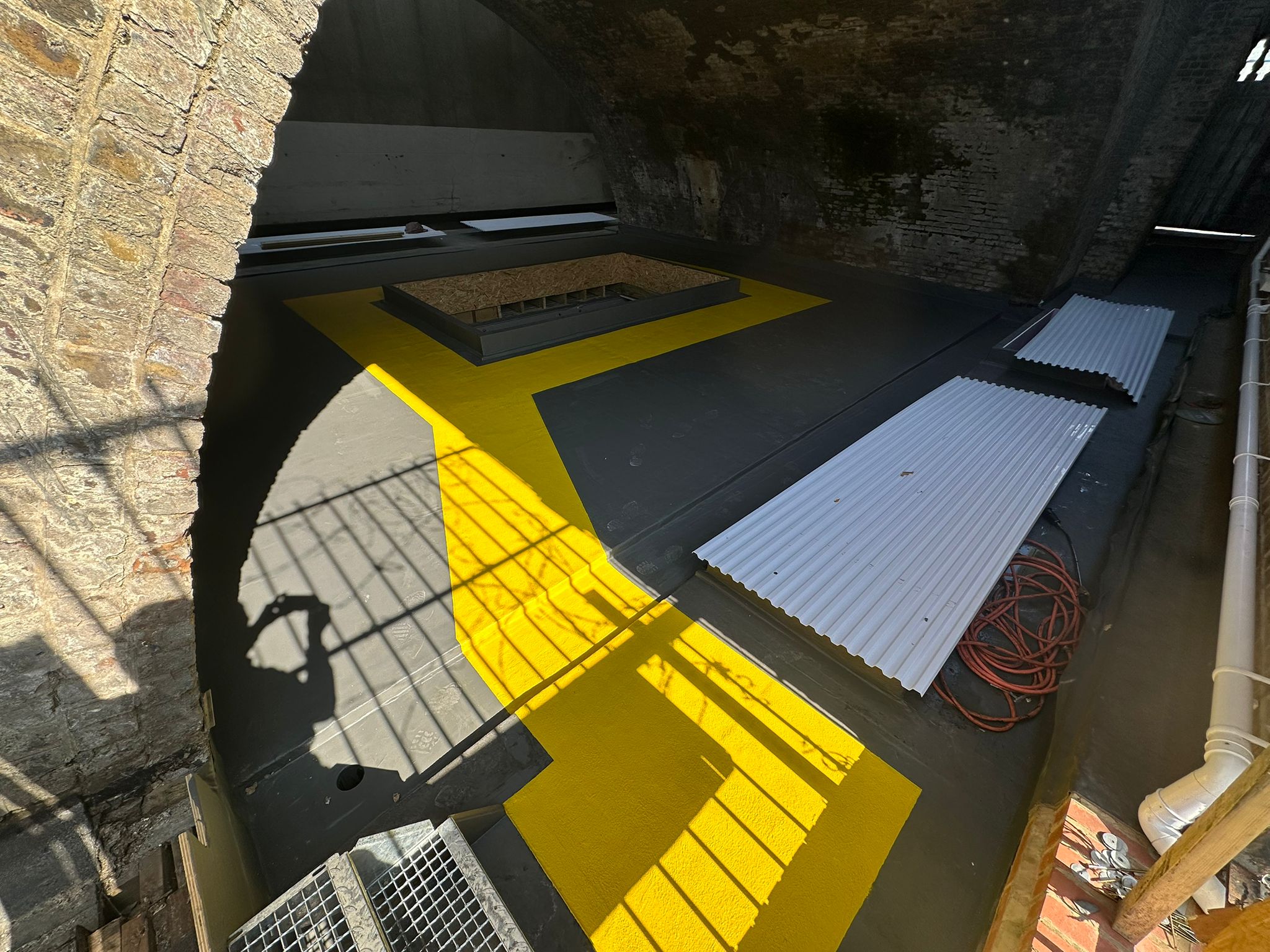 Underground chamber with yellow metal stairs leading down, blue corrugated panels on floor, stone walls and concrete surfaces visible.