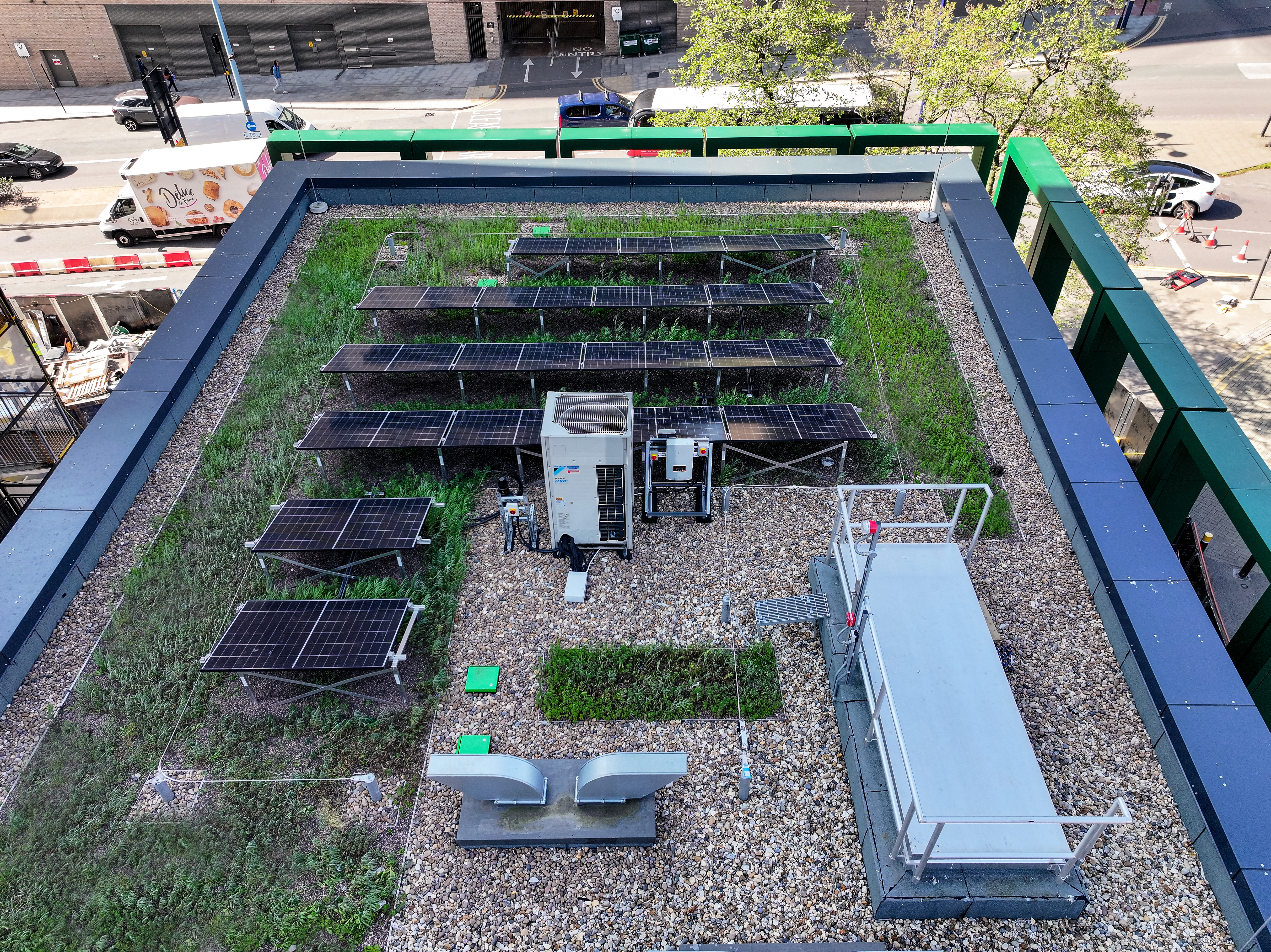 Aerial view of a rooftop with a green roof, solar panels, HVAC unit, and gravel sections on an urban building.