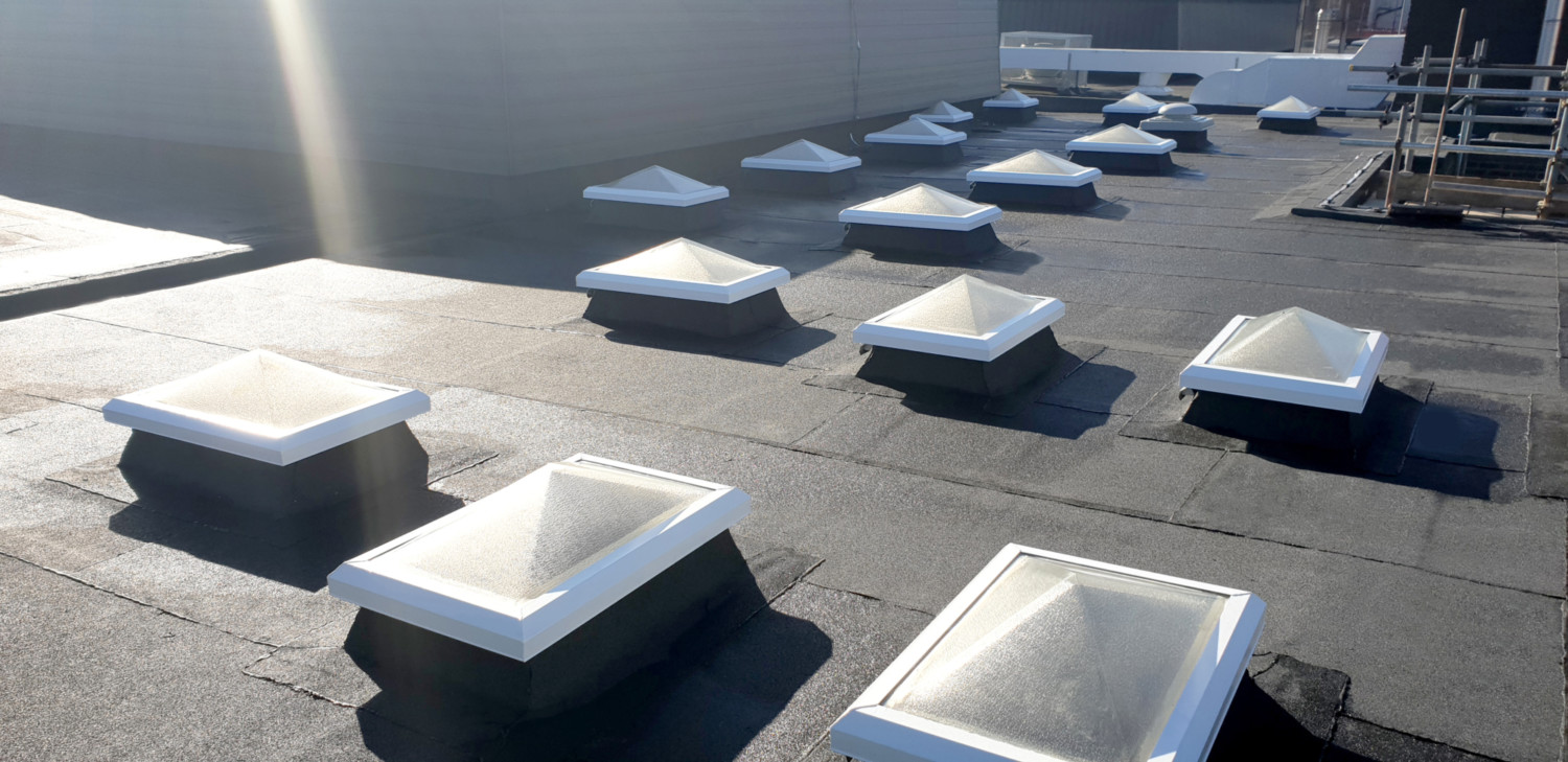 Multiple white square skylights installed on grey concrete roof surface with bright sunlight creating shadows.