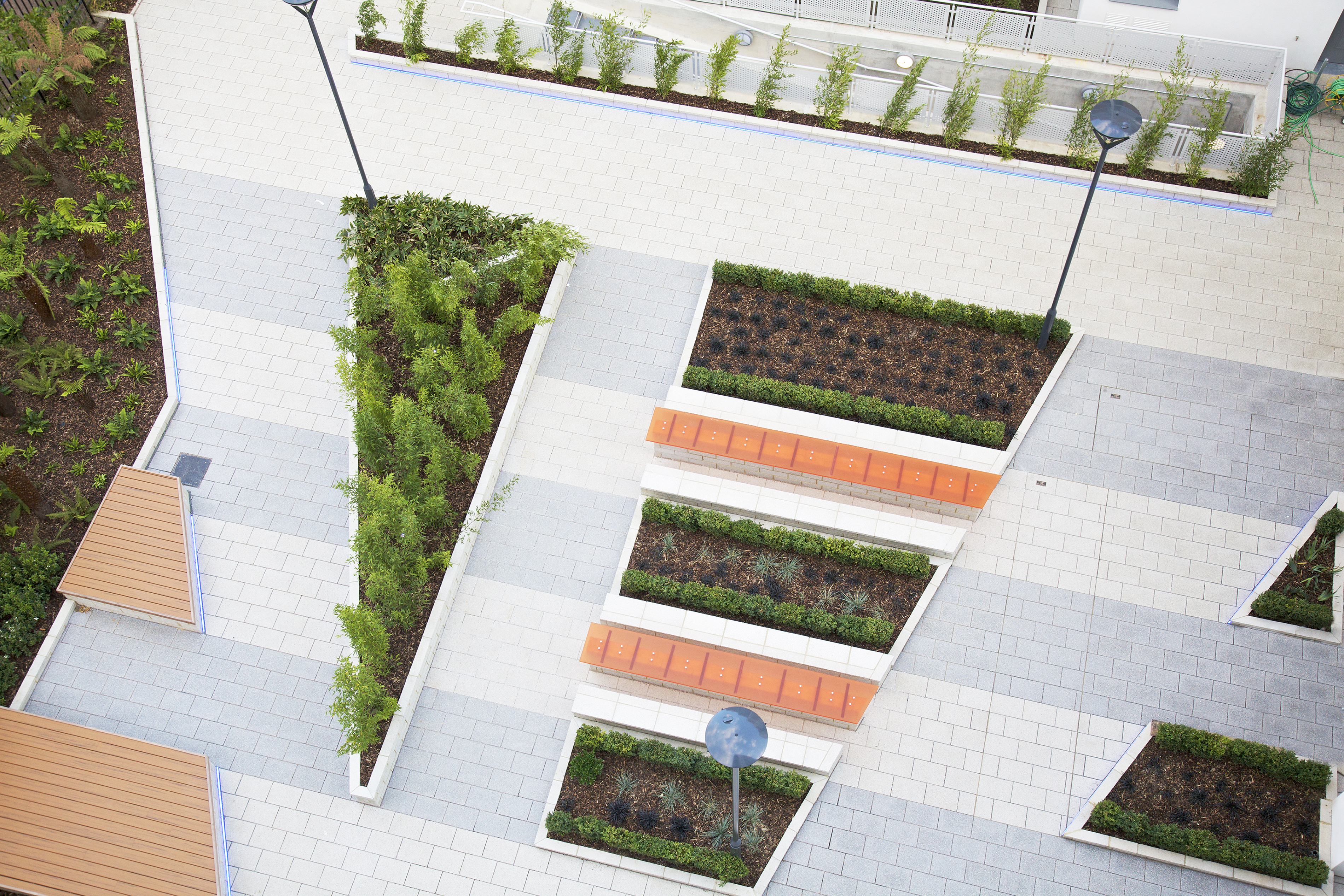 Aerial view of geometric garden with rectangular raised beds containing green plants, orange seating areas, and white paved pathways.