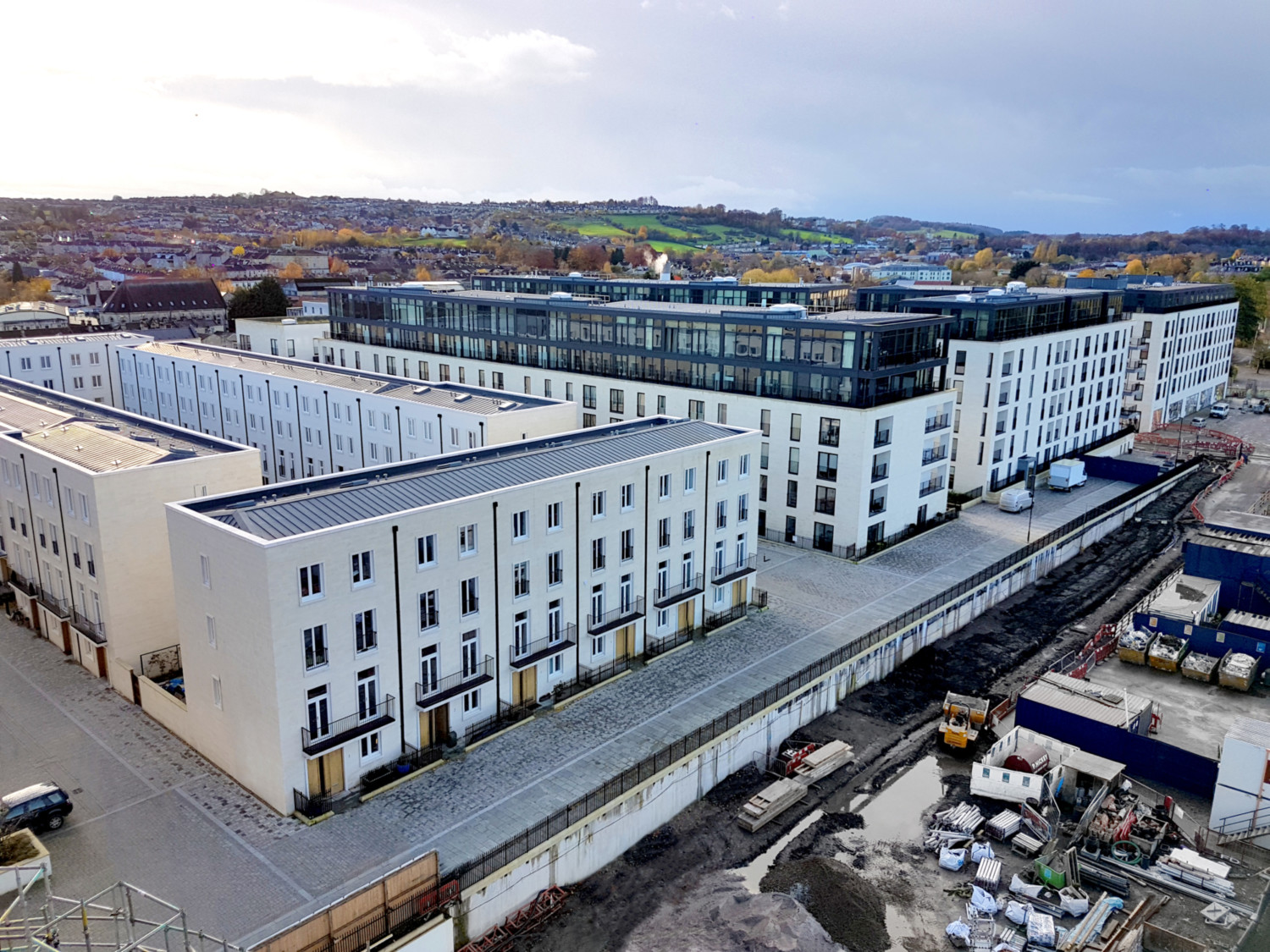 Aerial view of large modern white rectangular building complex with glass upper sections, surrounded by construction site and residential area.