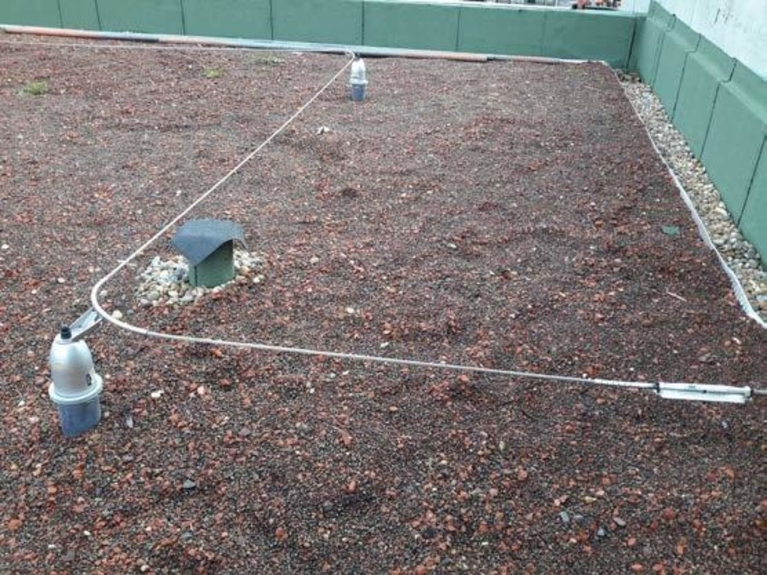 Flat roof with brown gravel surface, white rope marking rectangular perimeter, green metal box and white container visible.
