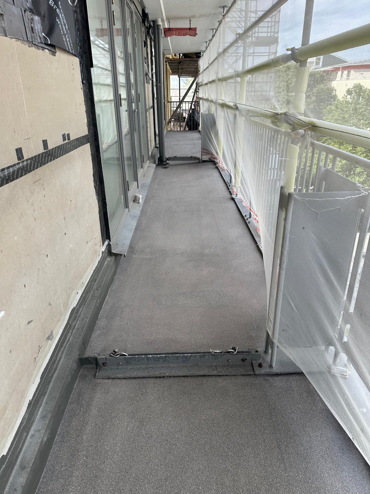 Construction walkway with white scaffolding railings, grey flooring, and protective sheeting covering building exterior.