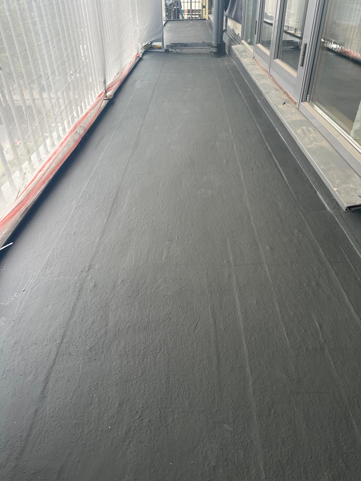 Flat roof terrace with dark waterproof membrane, red edging strips, and glass doors leading to interior spaces.