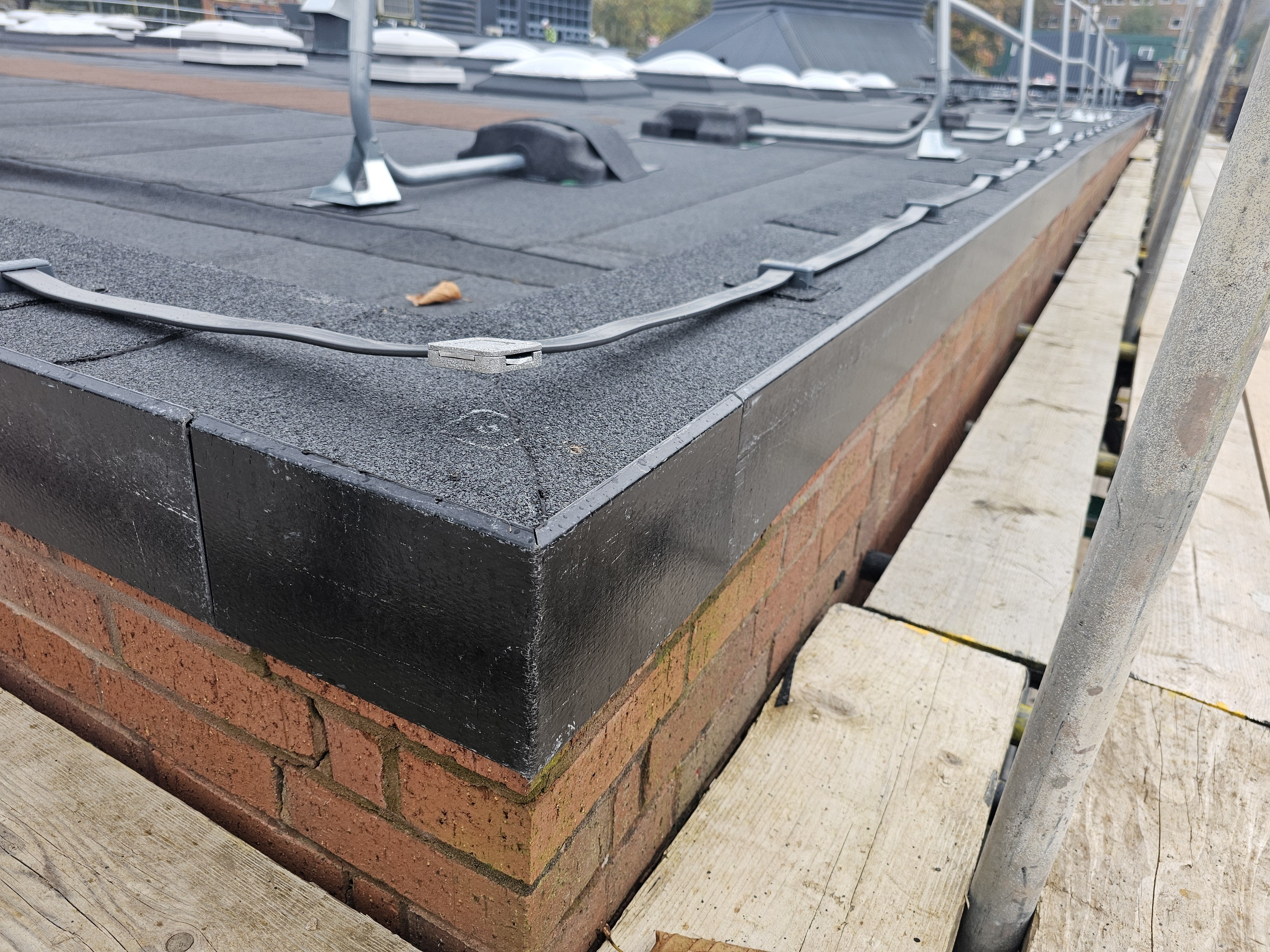 Flat roof with dark grey membrane covering, red brick parapet wall, wooden decking edge, metal fixtures and vents visible.