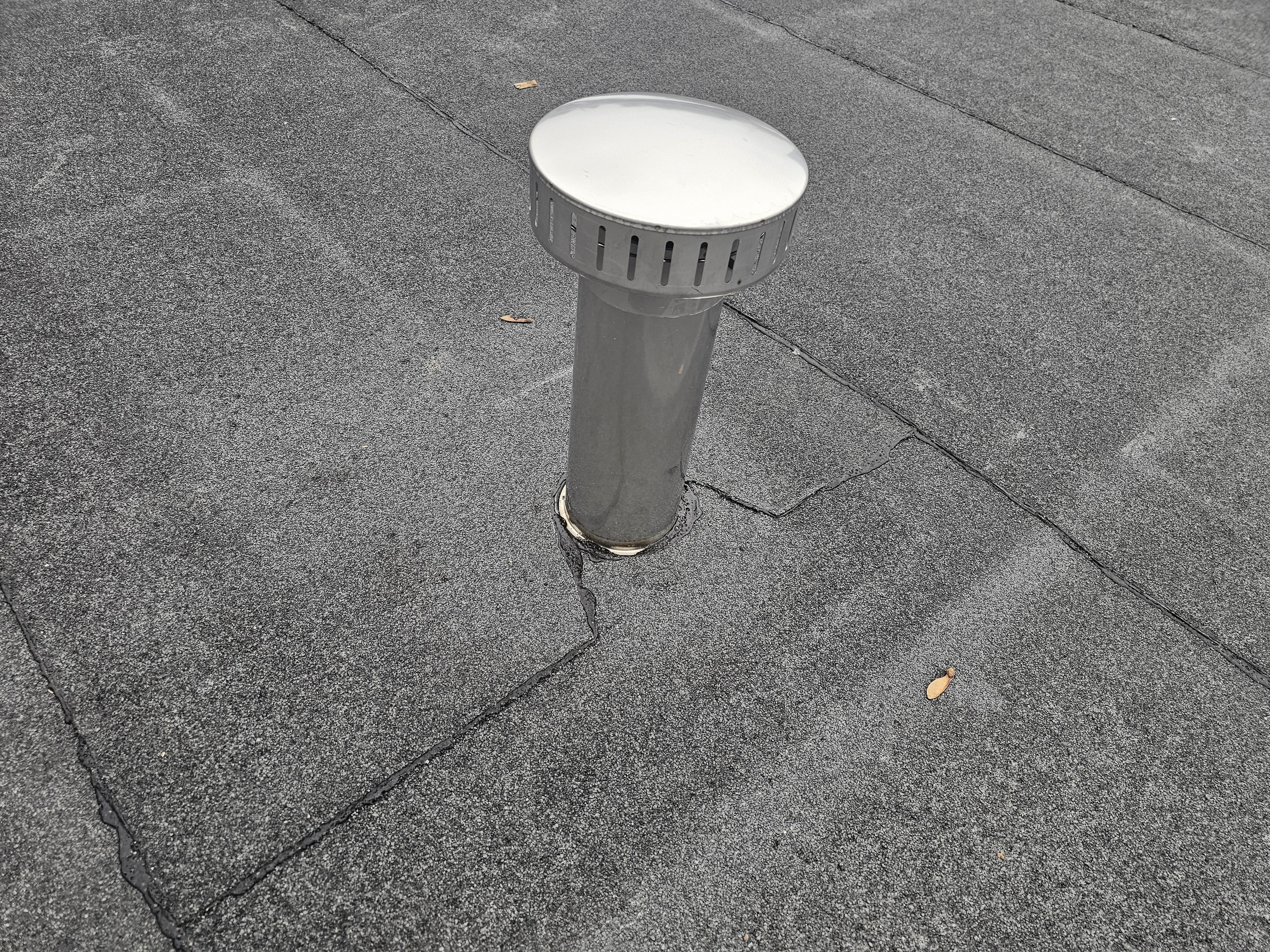 Grey cylindrical drain pipe with white circular top and ventilation slits protruding from dark paved surface with visible joint lines.