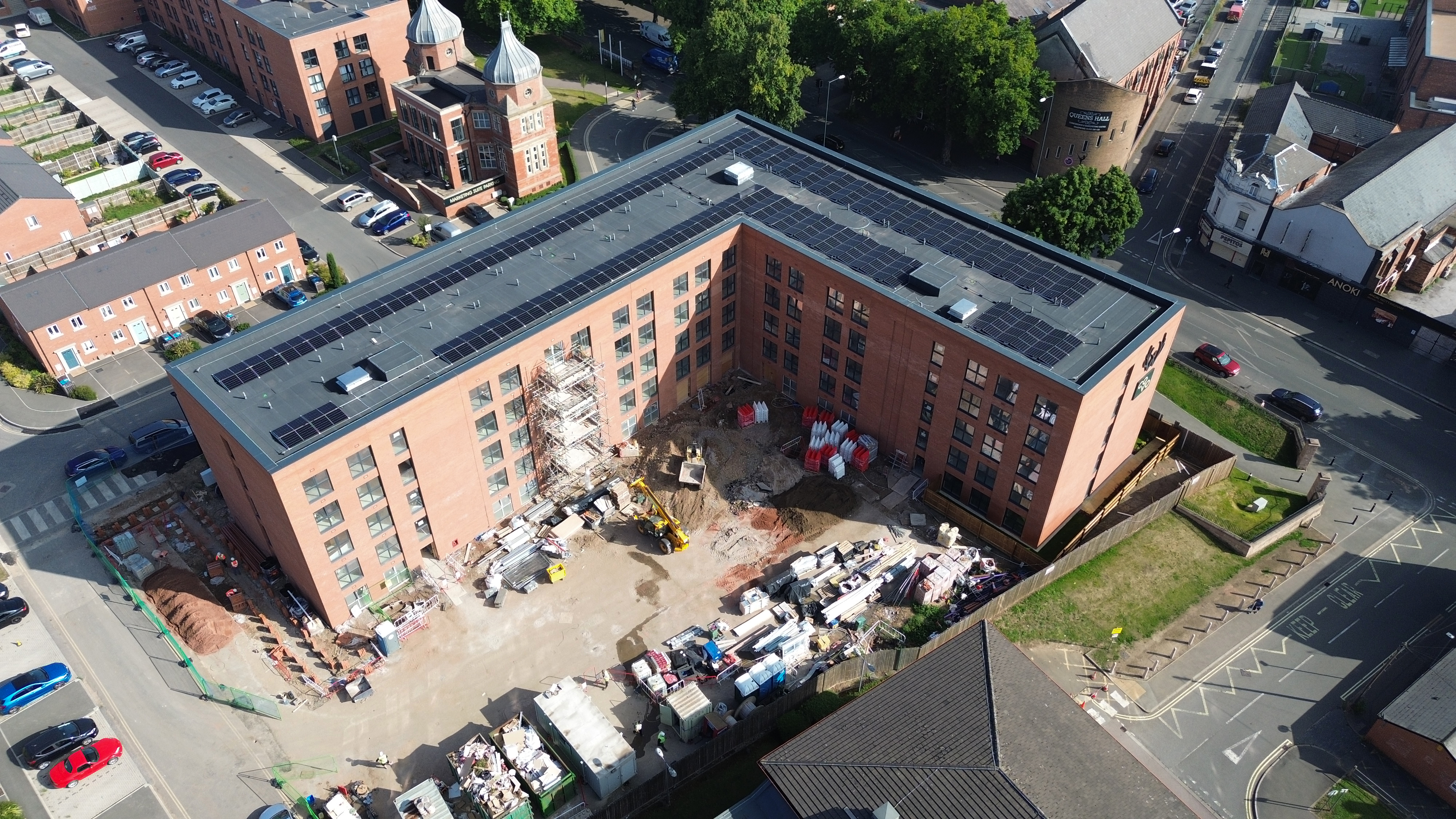 Aerial view of red brick residential building with partially collapsed roof section, debris scattered in central courtyard area.