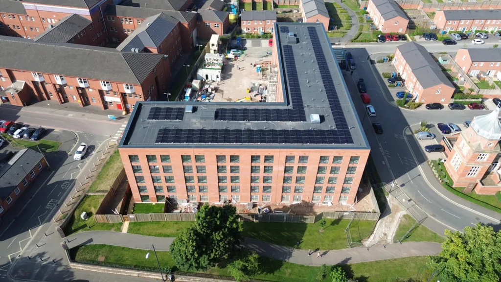 Aerial view of red brick residential building with dark grey roof, surrounded by housing estate with roads and green spaces.