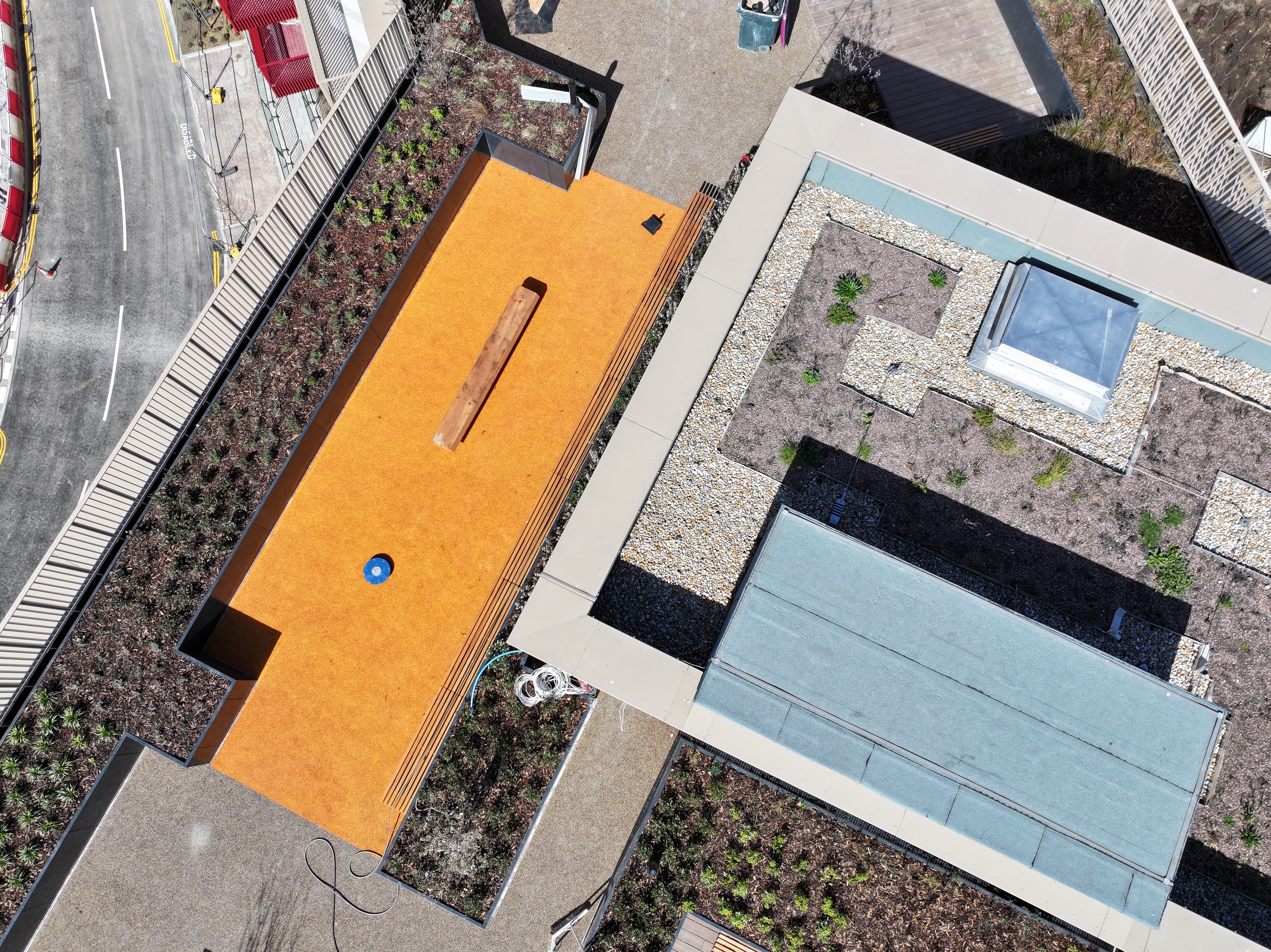 Aerial view of modern building with bright orange roof, rectangular pool, concrete pathways, and landscaped areas with vegetation.