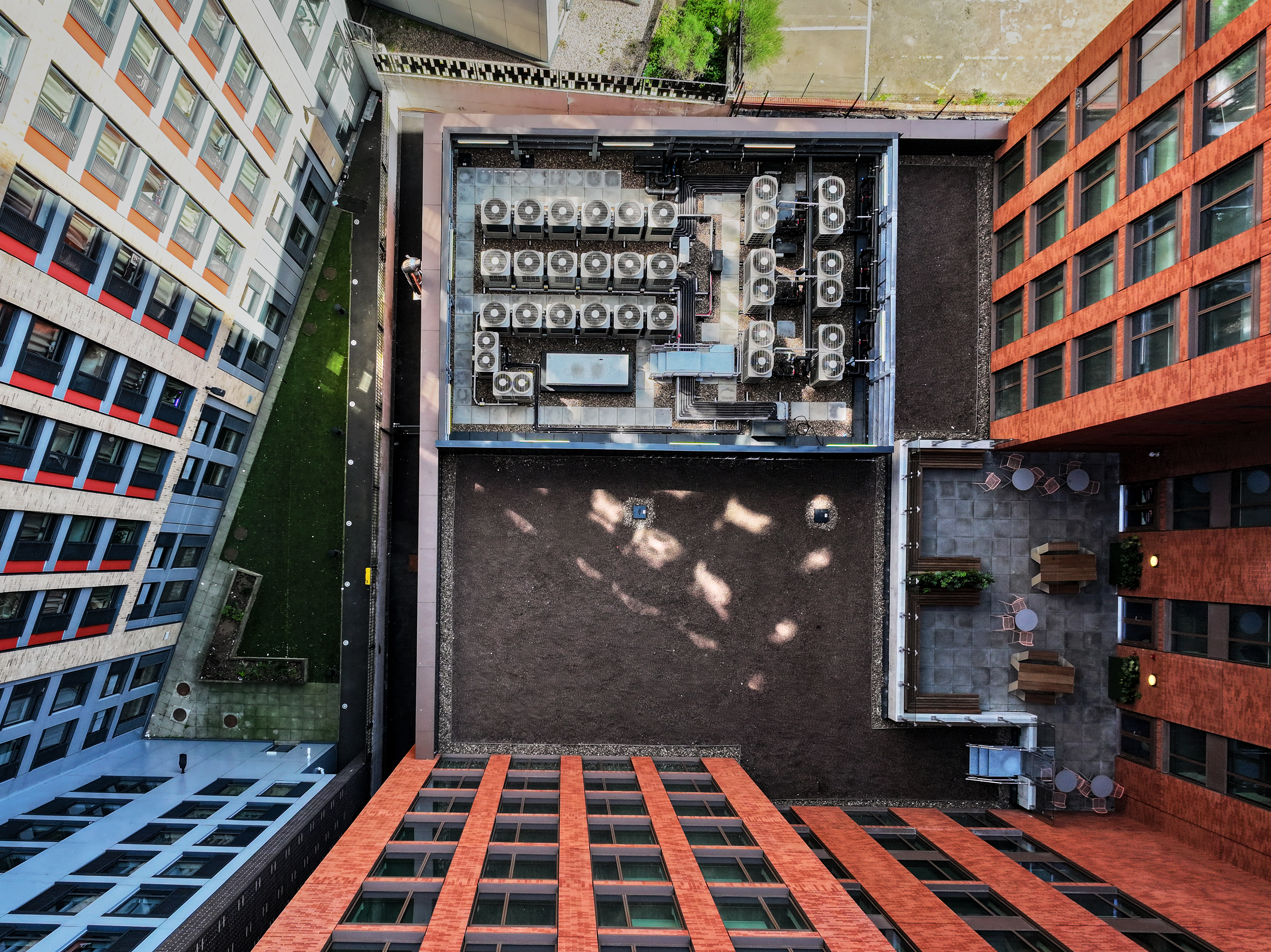 Aerial view looking down into a urban courtyard with rooftop HVAC units, surrounded by buildings with red and grey facades.