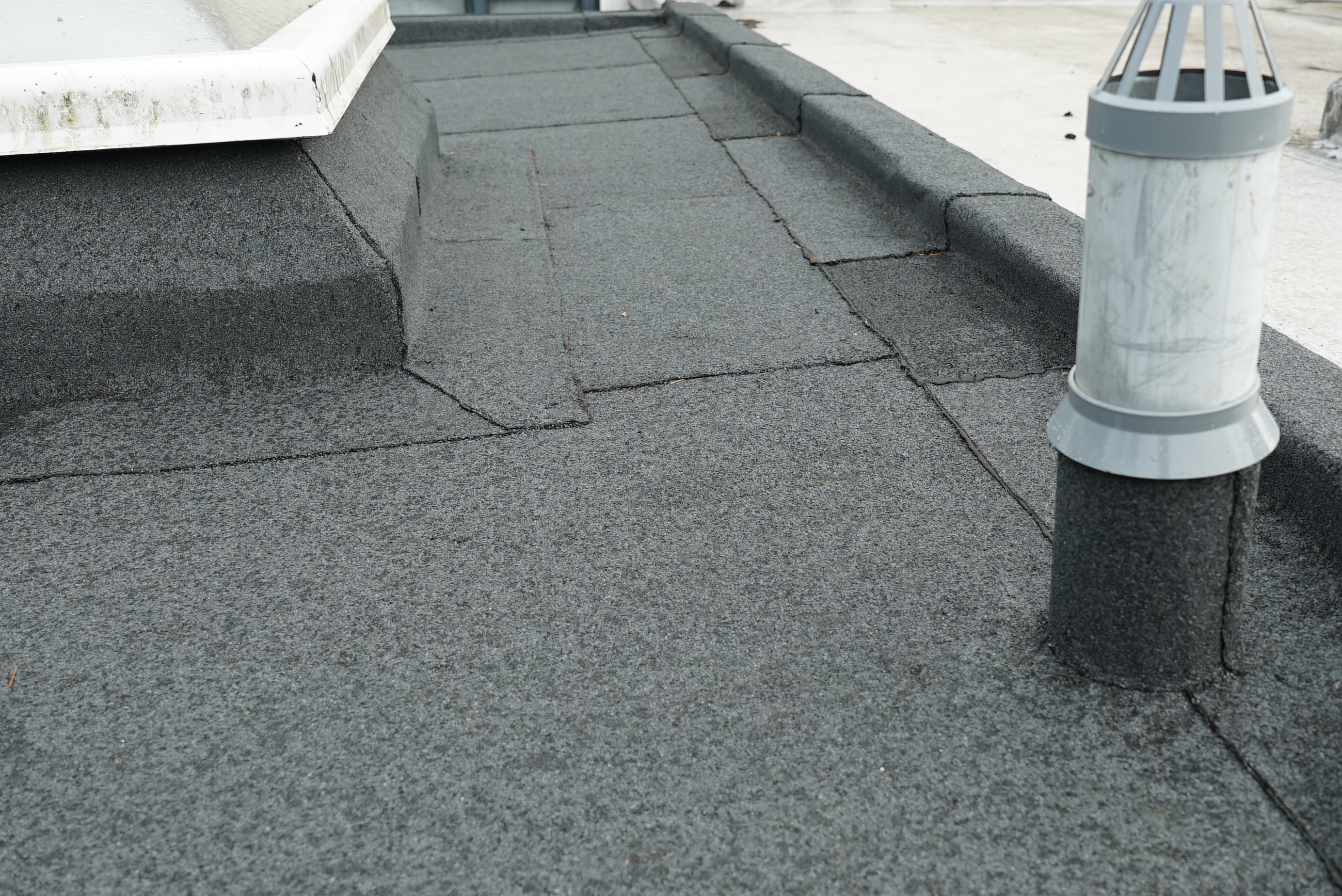 Flat roof with grey waterproof membrane, white ventilation pipes and equipment visible on surface.