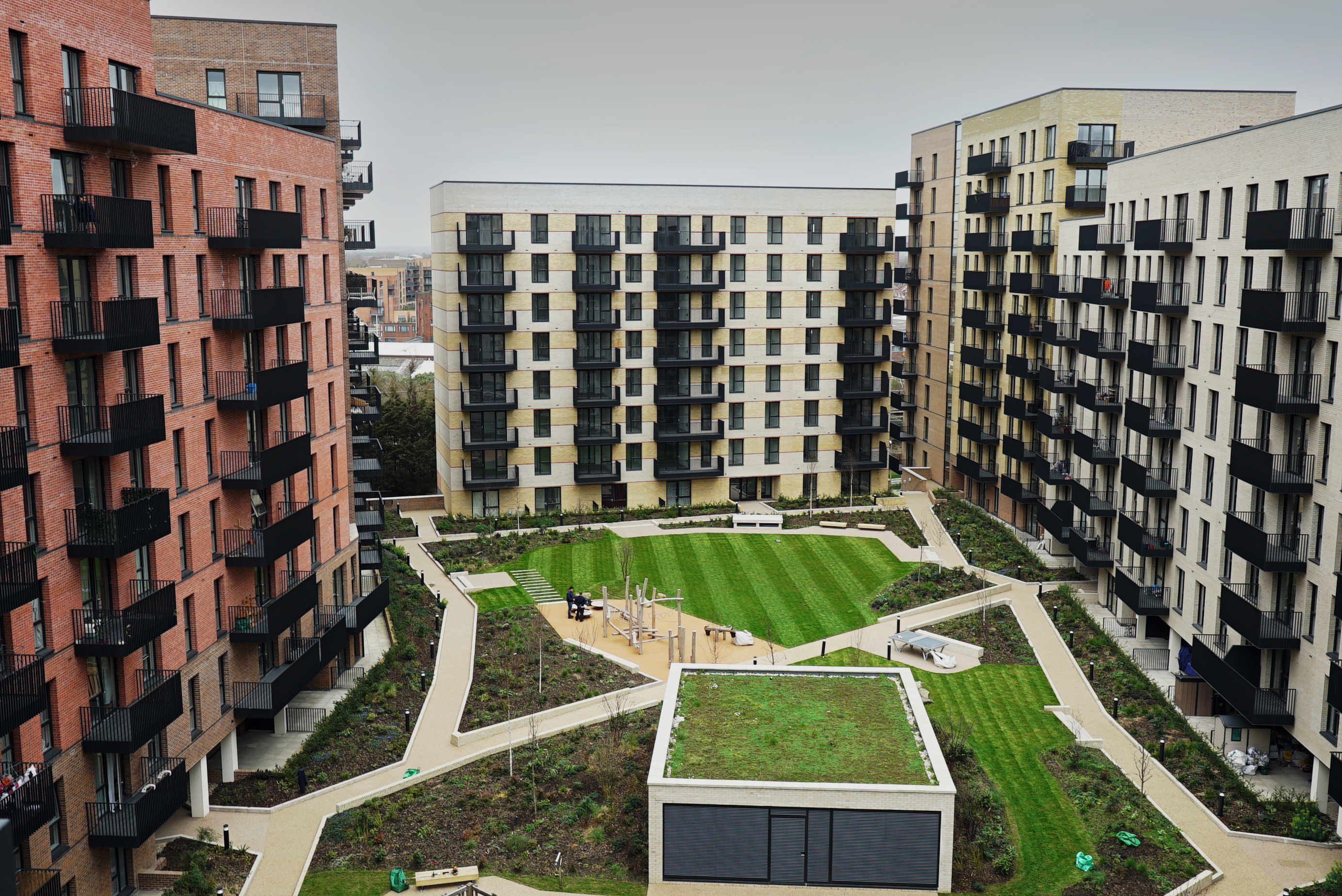 Aerial view of a modern residential courtyard with green lawn, pathways, play area, and surrounding multi-storey apartment blocks with balconies.