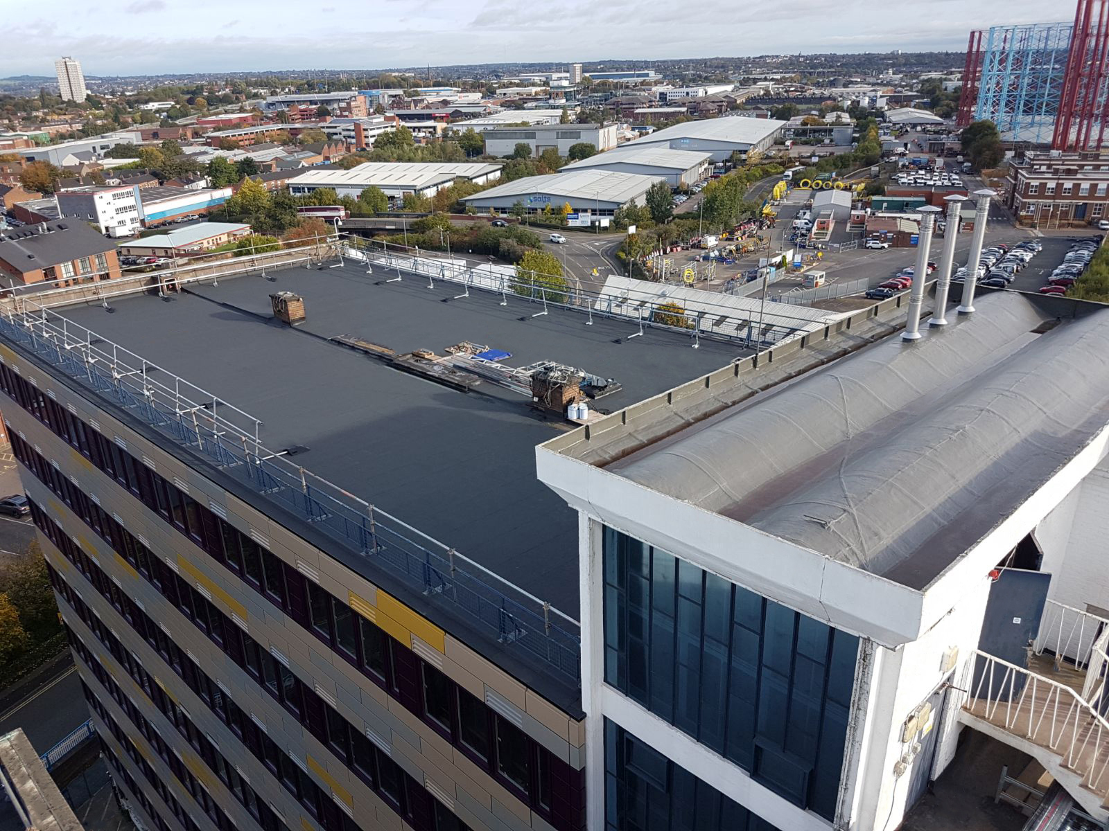 Aerial view of concrete rooftop with construction equipment, overlooking urban landscape with industrial buildings and car parks.