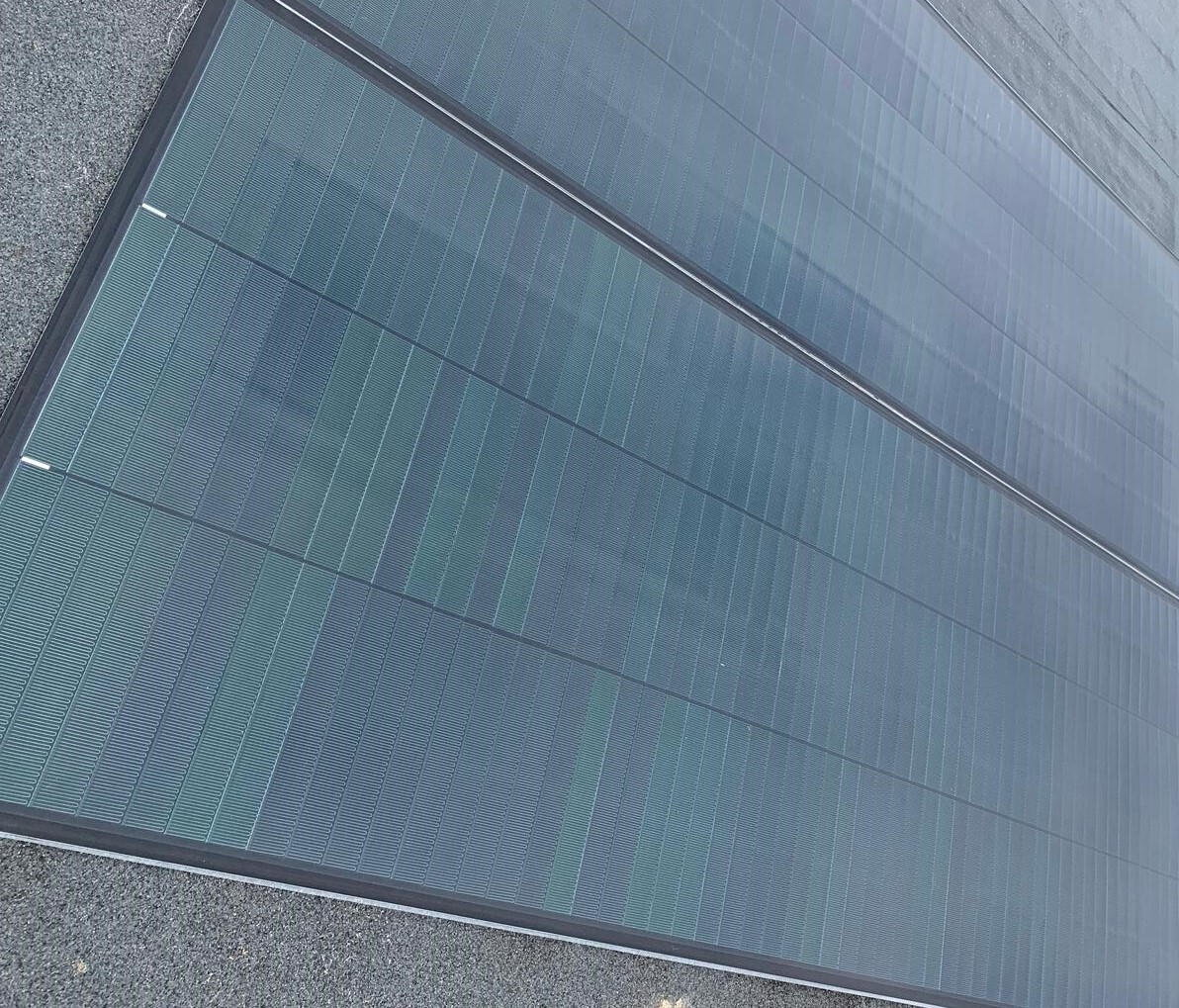 Glass-panelled building facade with reflective blue-green surface showing geometric rectangular sections and metal framing elements.