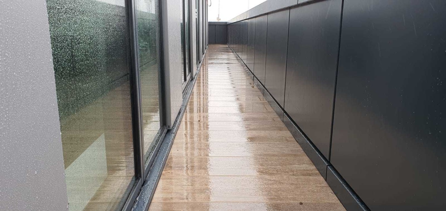 Long corridor with polished marble floors, glass walls on left, dark panelled walls on right, fluorescent ceiling lighting.