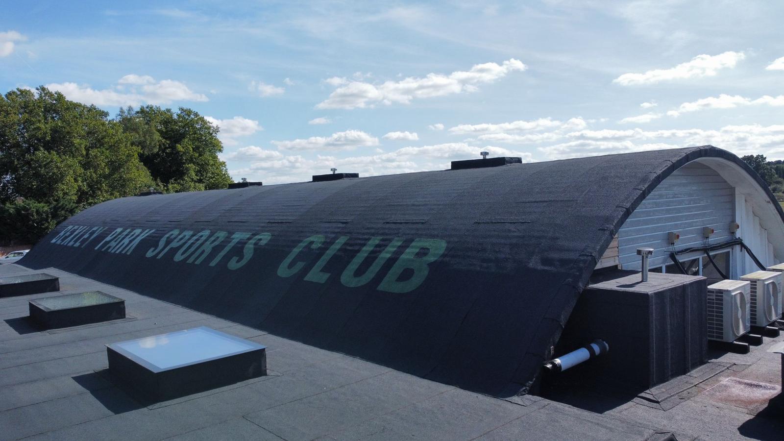 Large curved grey hangar with "MEMPHIS BLUES CLUB" text painted on side, white rectangular skylights on roof, blue sky with clouds.