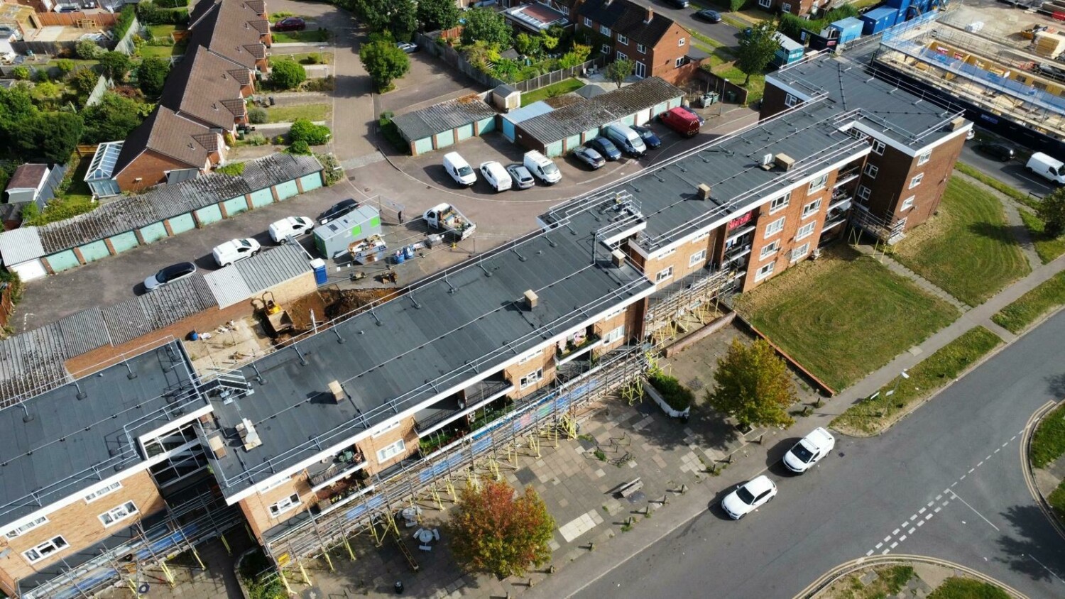 Aerial view of large brick school building with dark roof, surrounding car parks, residential houses, and green spaces.