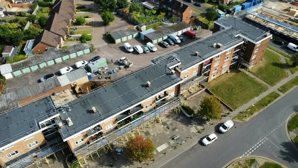 Aerial view of single-storey brick building with dark roof, surrounded by car parks, residential houses, and green spaces.