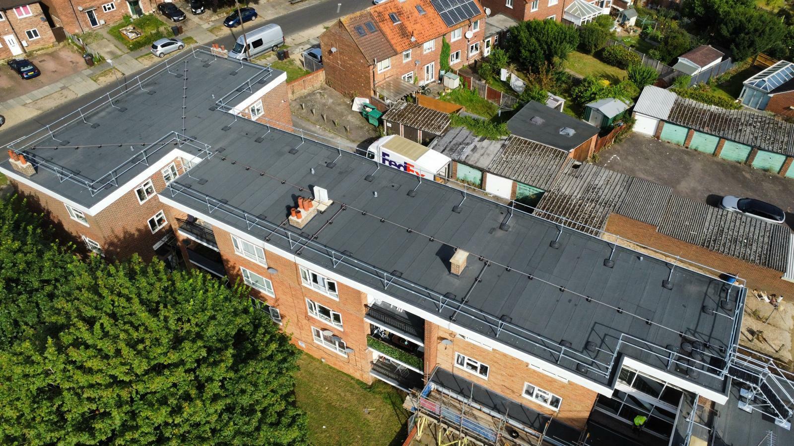 Aerial view of brick residential building with grey roof surrounded by houses, gardens, and trees in suburban neighbourhood.