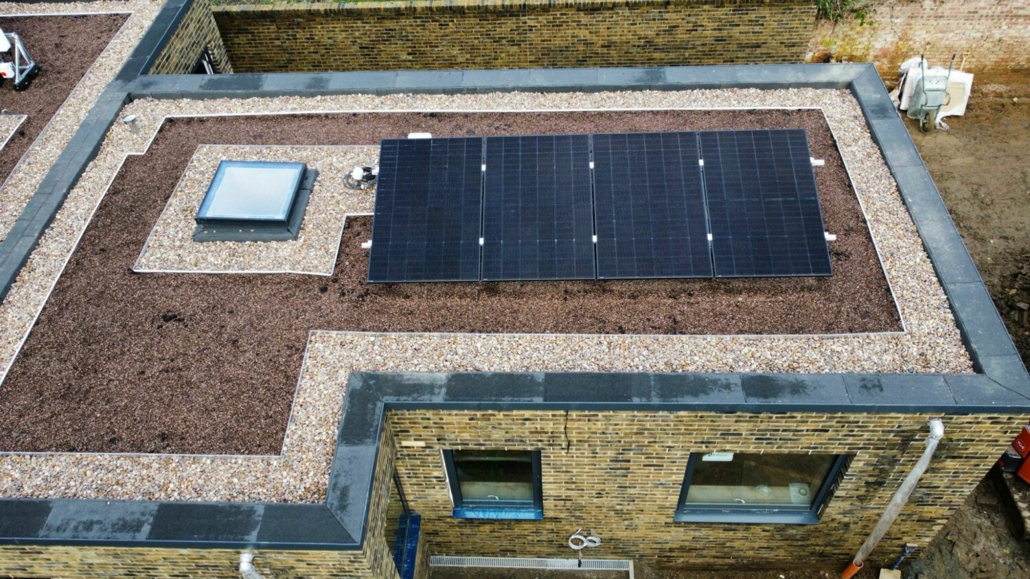 Aerial view of flat roof with dark solar panels arranged in rectangular grid, surrounded by gravel and brick building below.