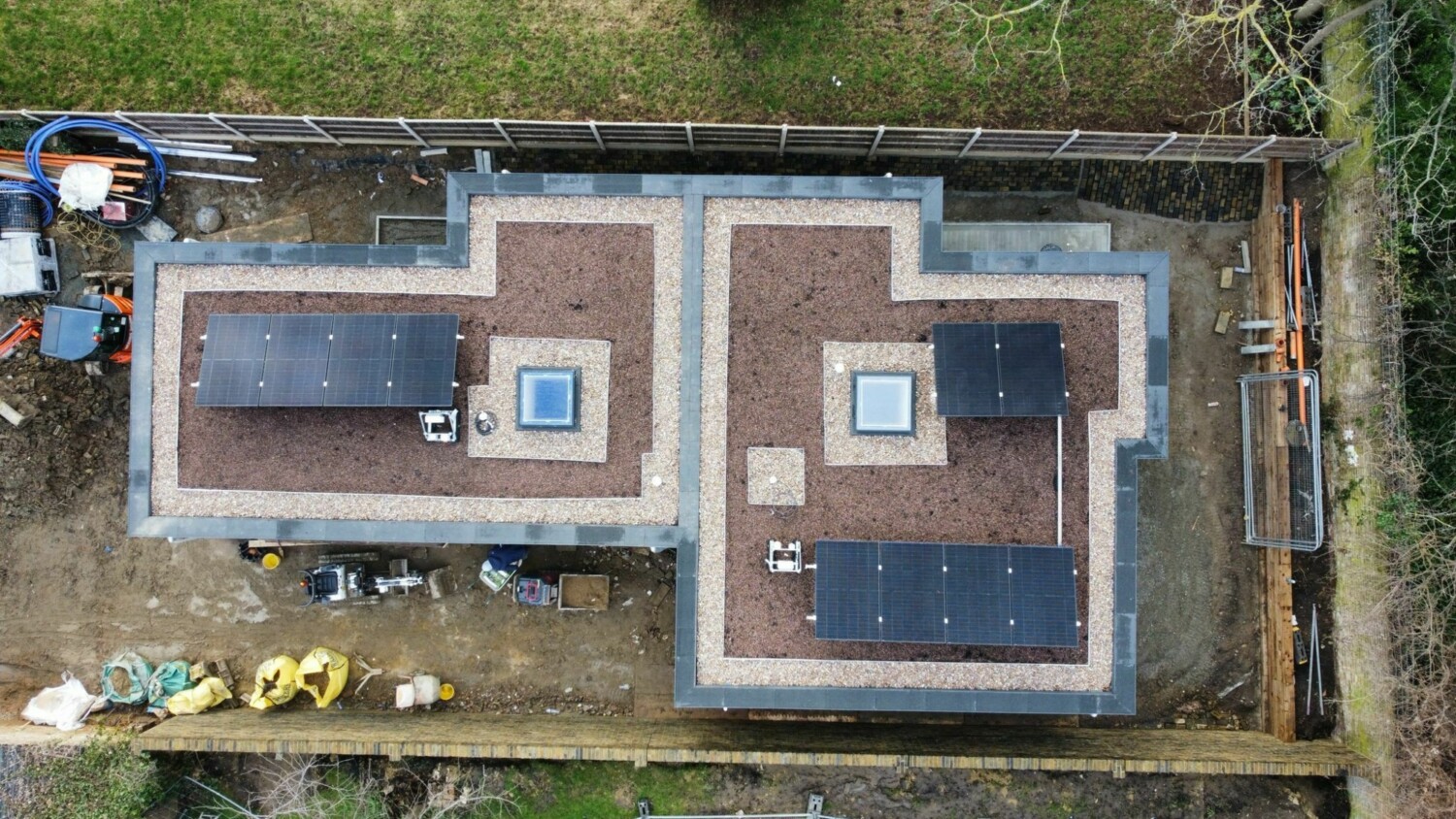 Aerial view of construction site showing two rectangular concrete structures with dark roofing sections and central square openings.