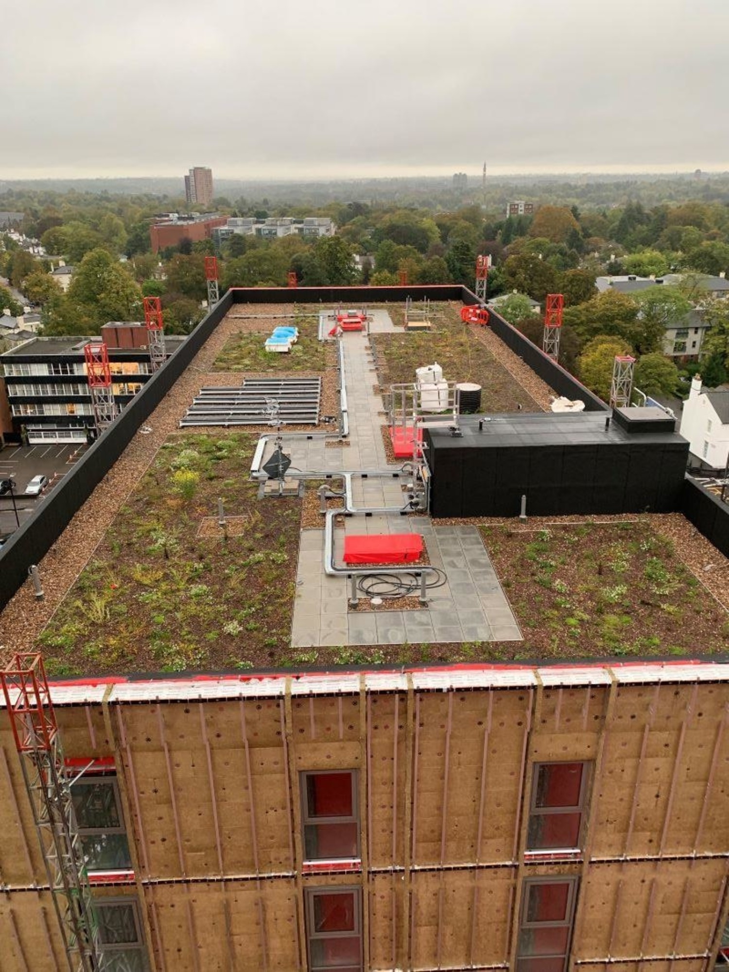 Aerial view of green roof with vegetation patches, solar panels, and red ventilation units on wooden residential building.