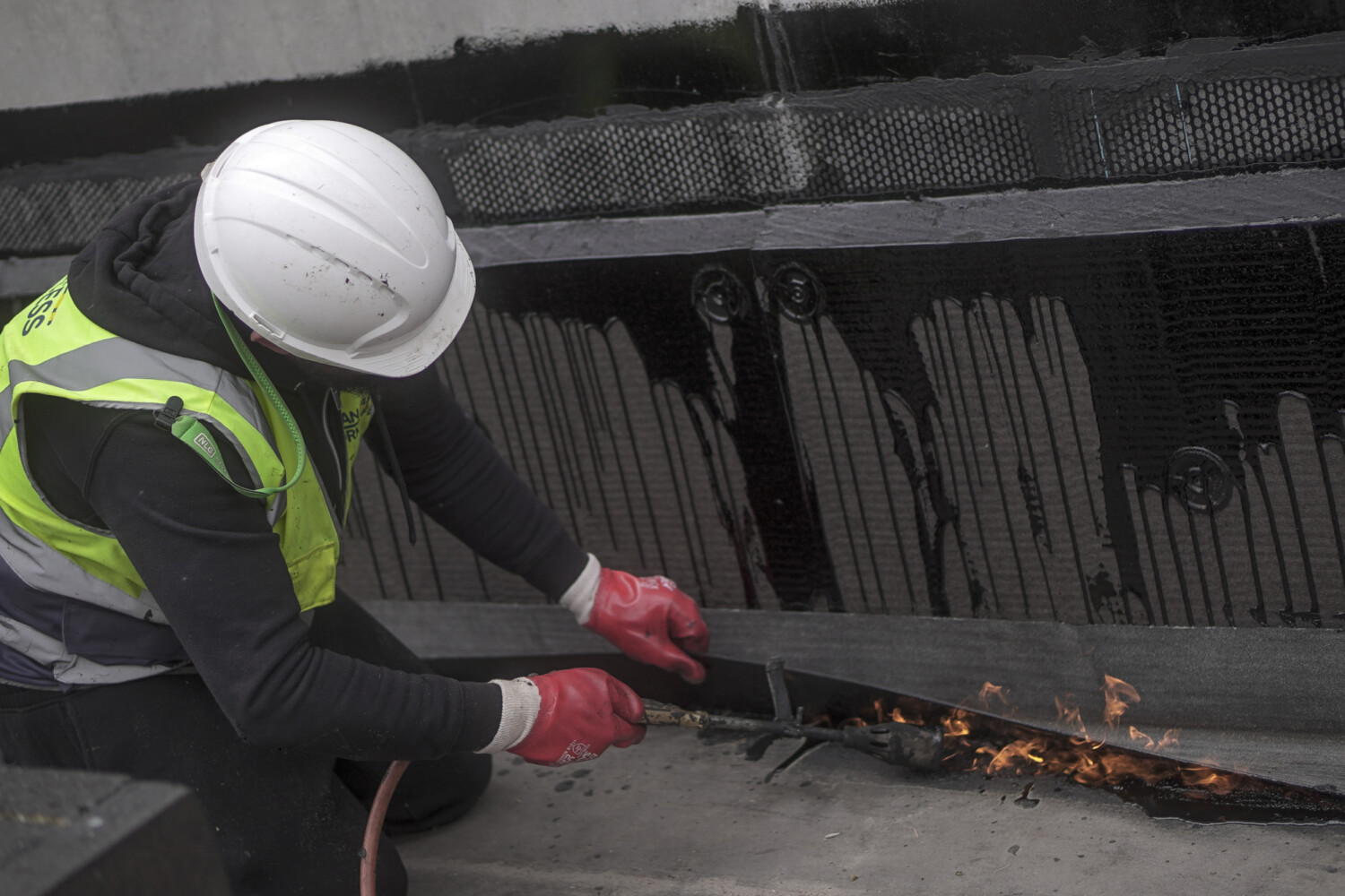 Construction worker in white hard hat and high-vis jacket using welding torch on metal railway track, creating sparks.