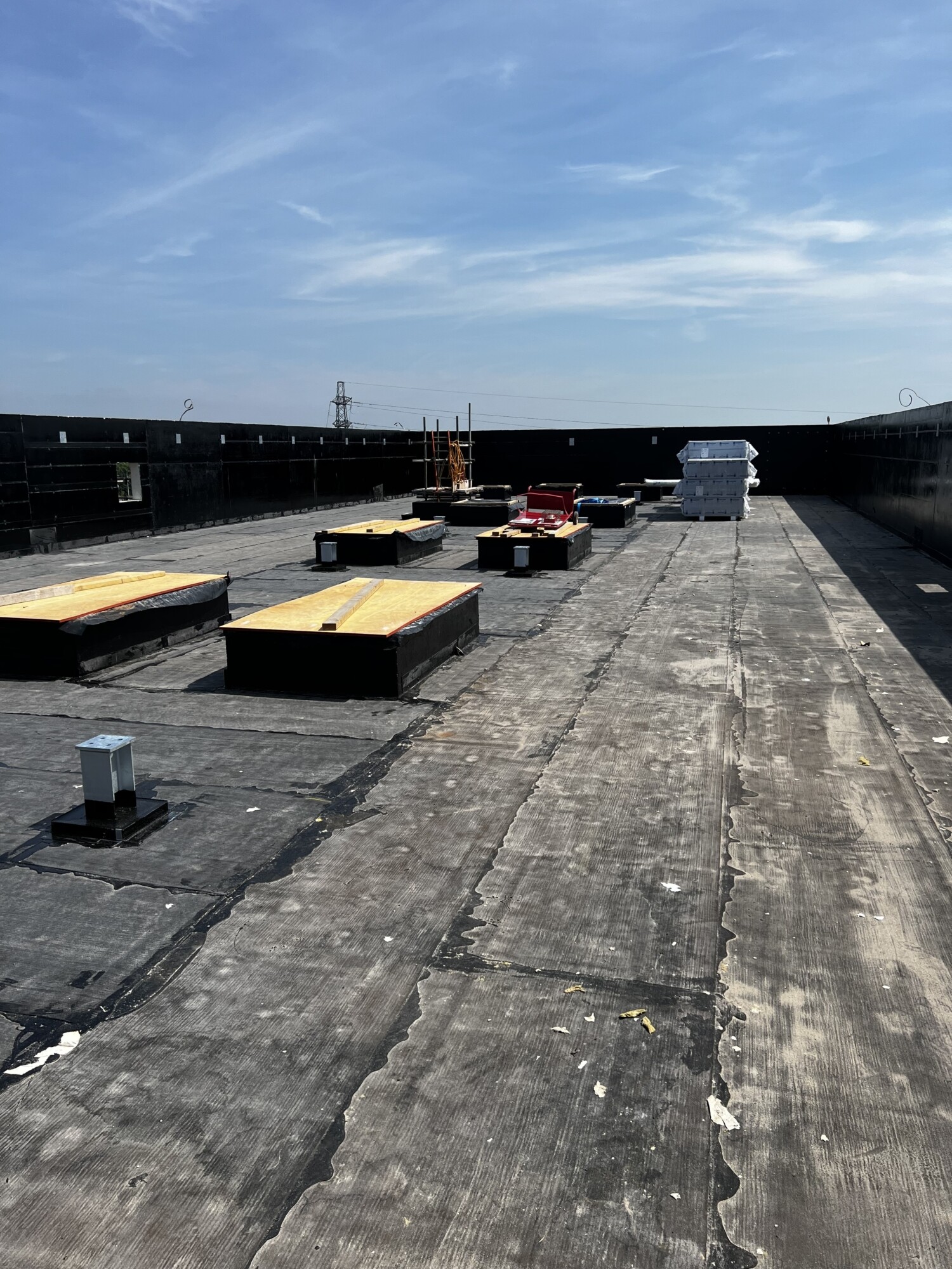 Concrete rooftop with yellow and red air conditioning units, weathered surface, low walls, and blue sky with white clouds above.