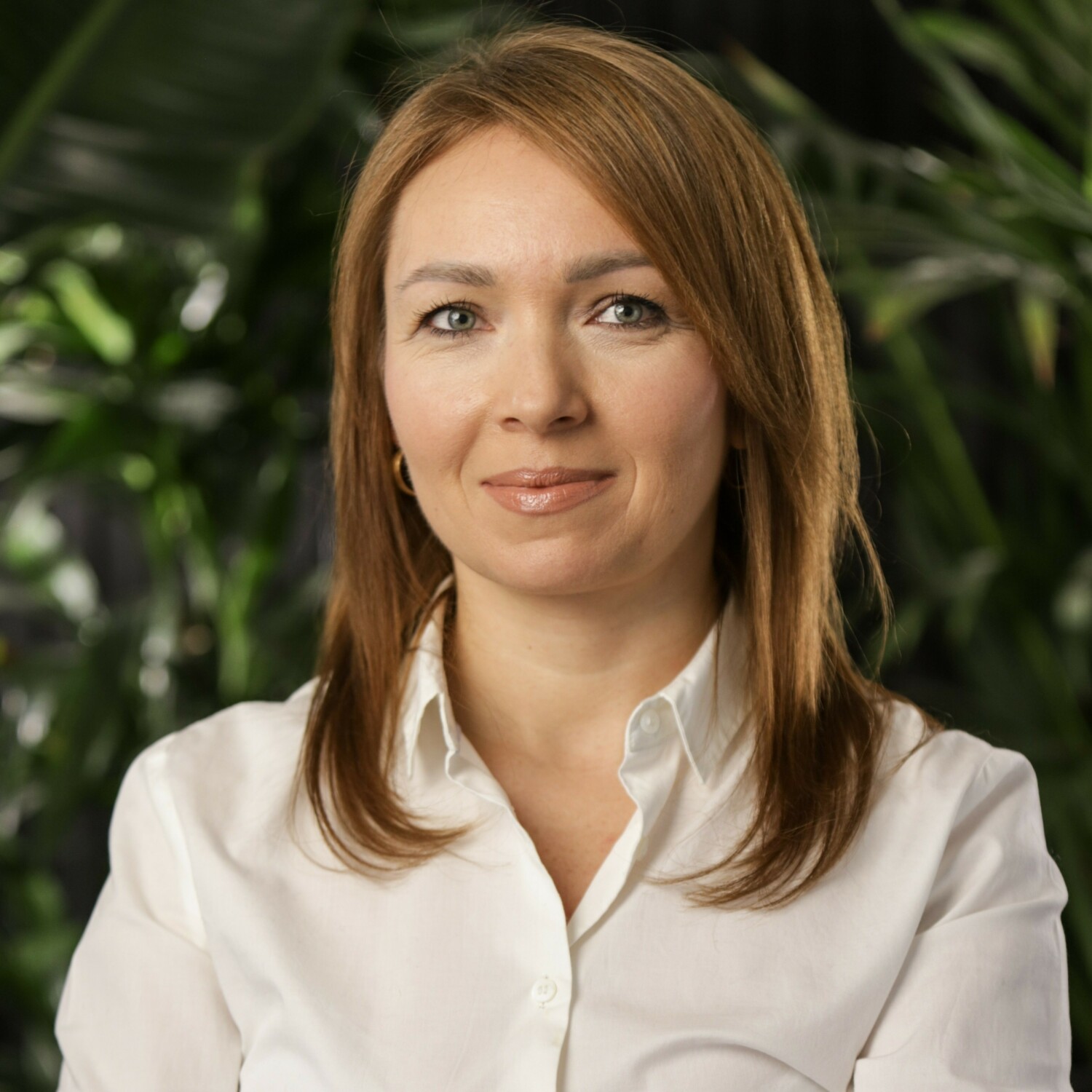 Woman with shoulder-length brown hair wearing white collared shirt, green foliage background