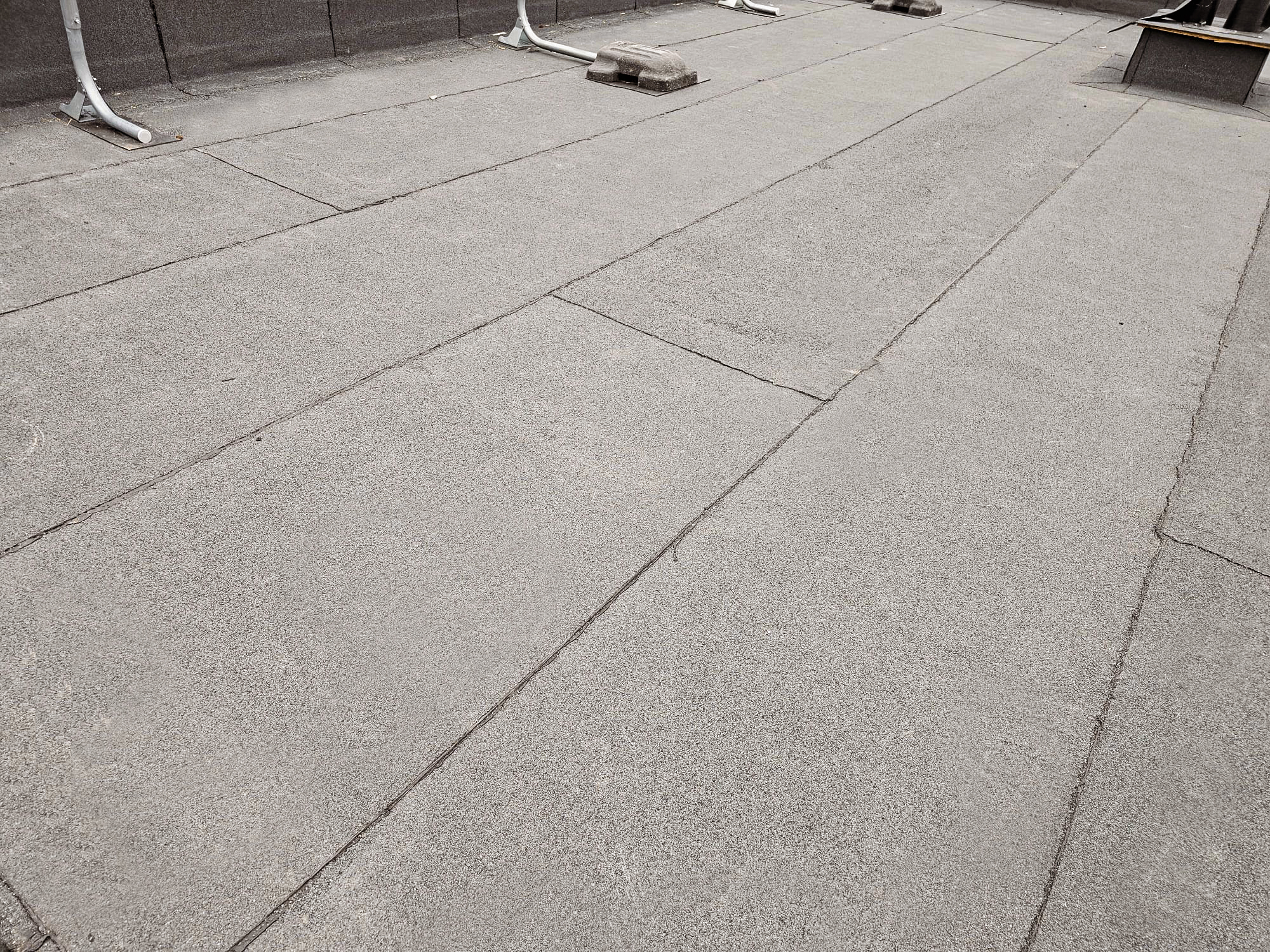 Large grey concrete paving slabs on an outdoor terrace, with white metal furniture legs and a small raised fixture visible in the background.