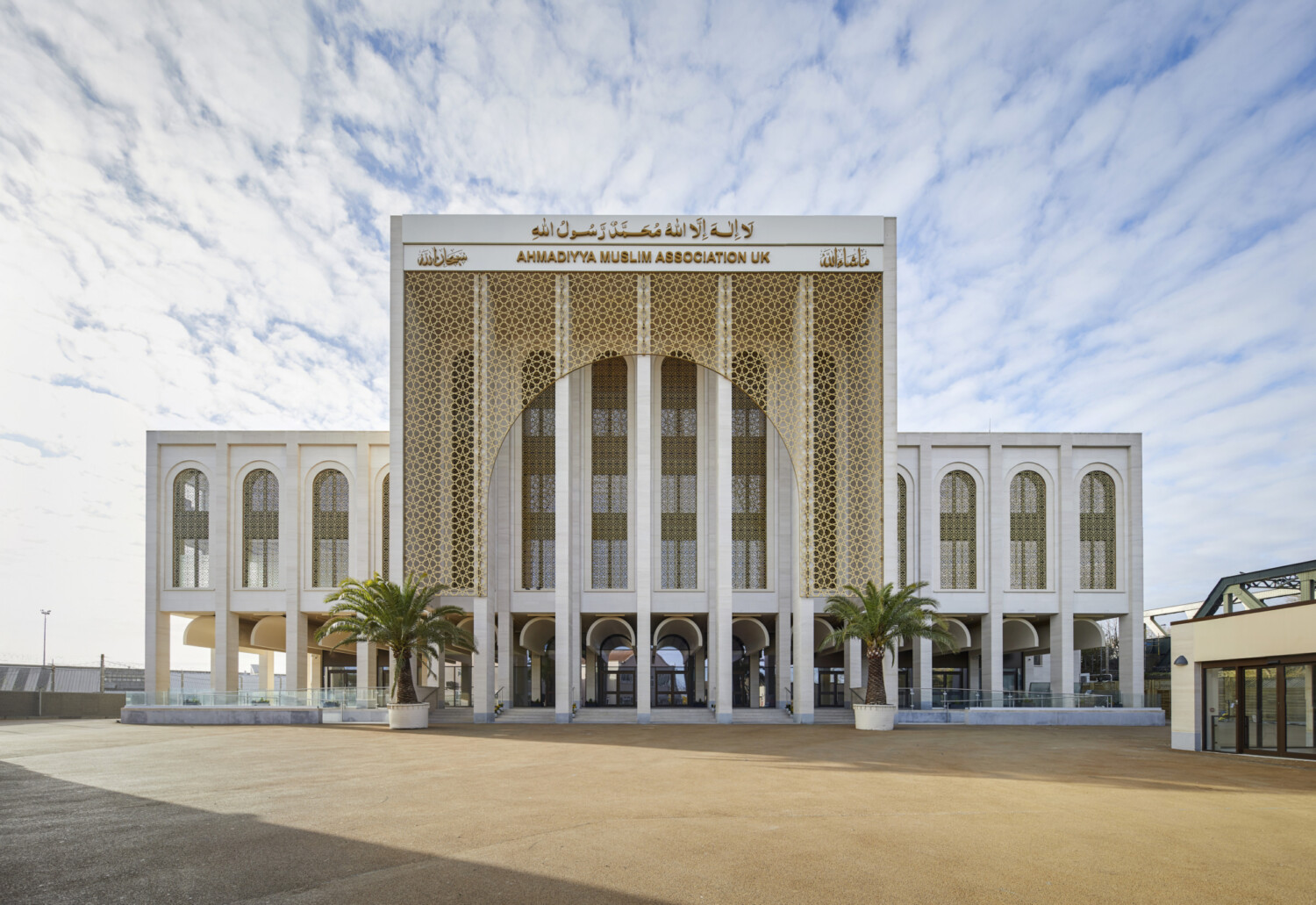 White modern building with ornate golden geometric patterns on central facade, flanked by symmetrical wings with arched windows.