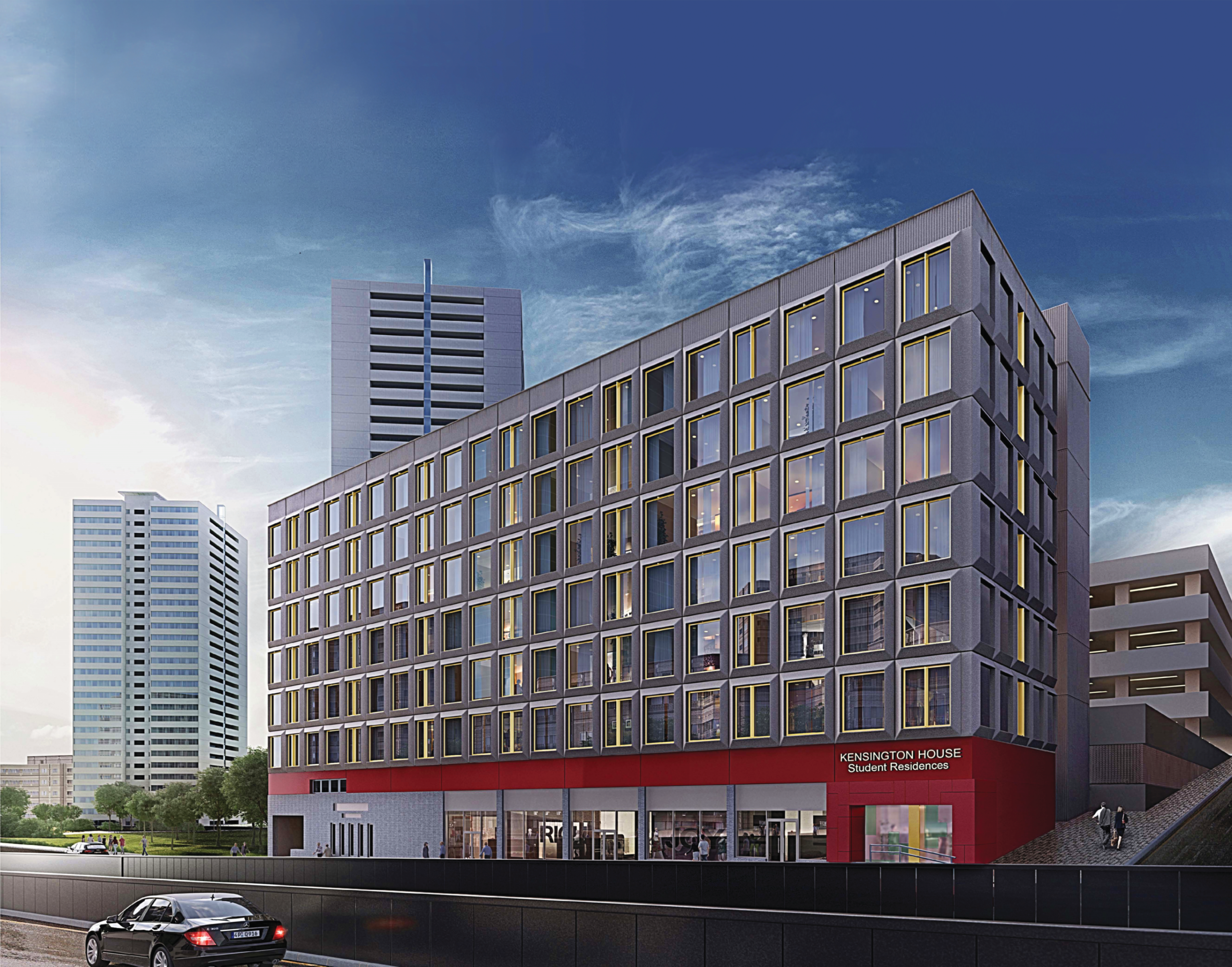 Modern grey rectangular building with red ground floor retail space, surrounded by white tower blocks under blue cloudy sky.