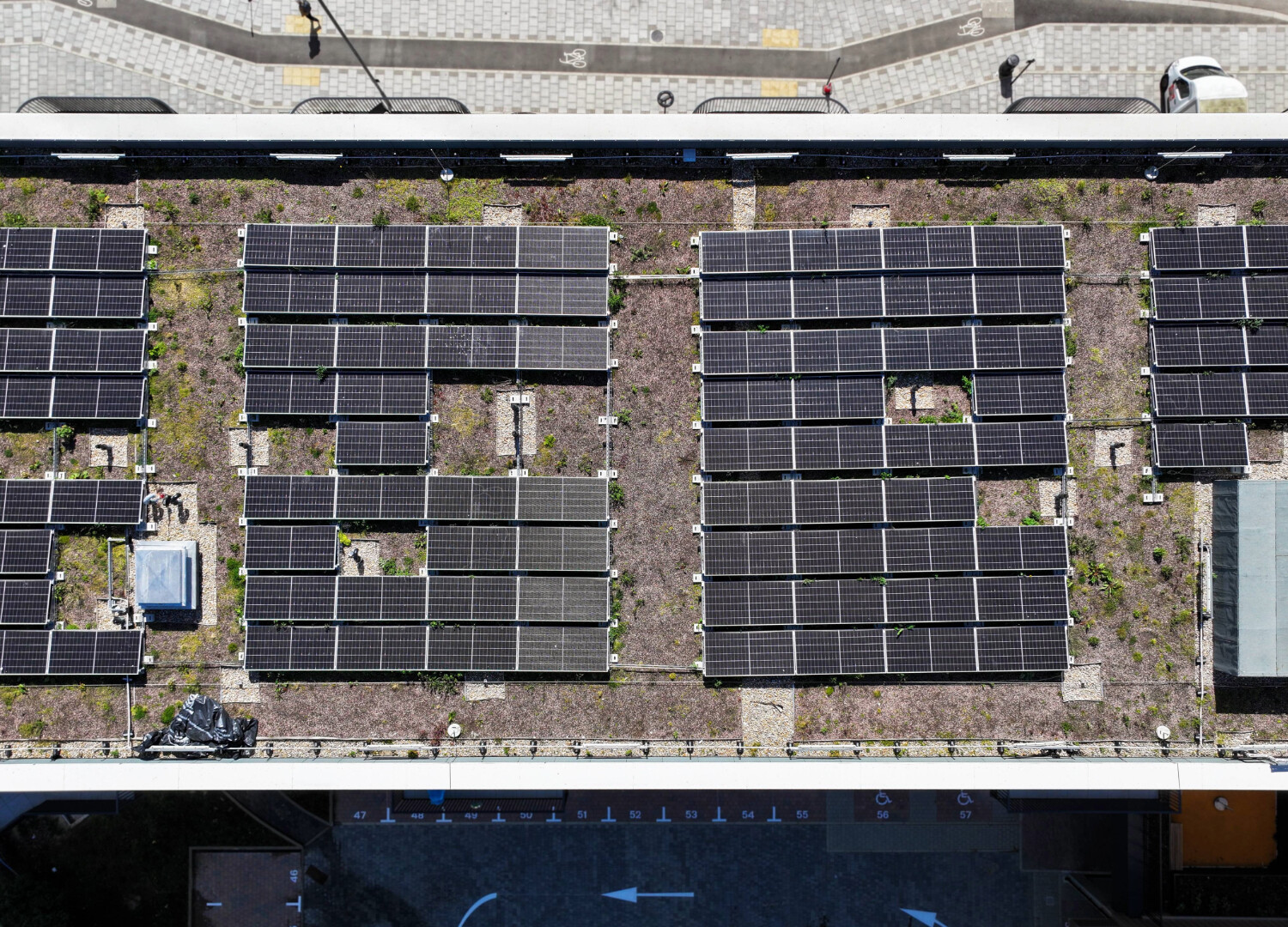 Aerial view of dark solar panels arranged in rows on brown ground between two roads with white markings.