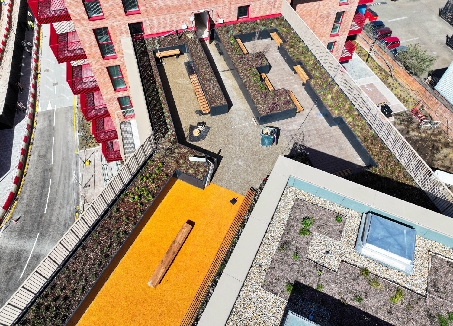 Aerial view of residential buildings with red brick facades, orange sports court, swimming pool, and landscaped courtyards.