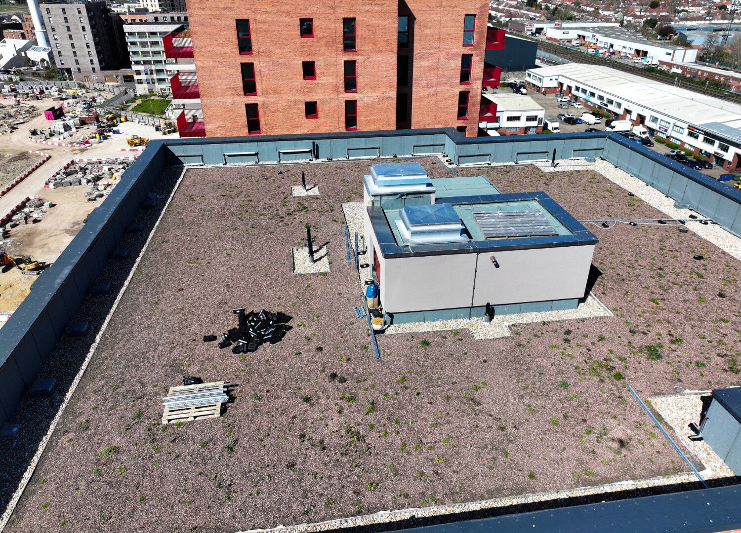 Aerial view of flat rooftop with white HVAC units, gravel surface, and red brick building in background