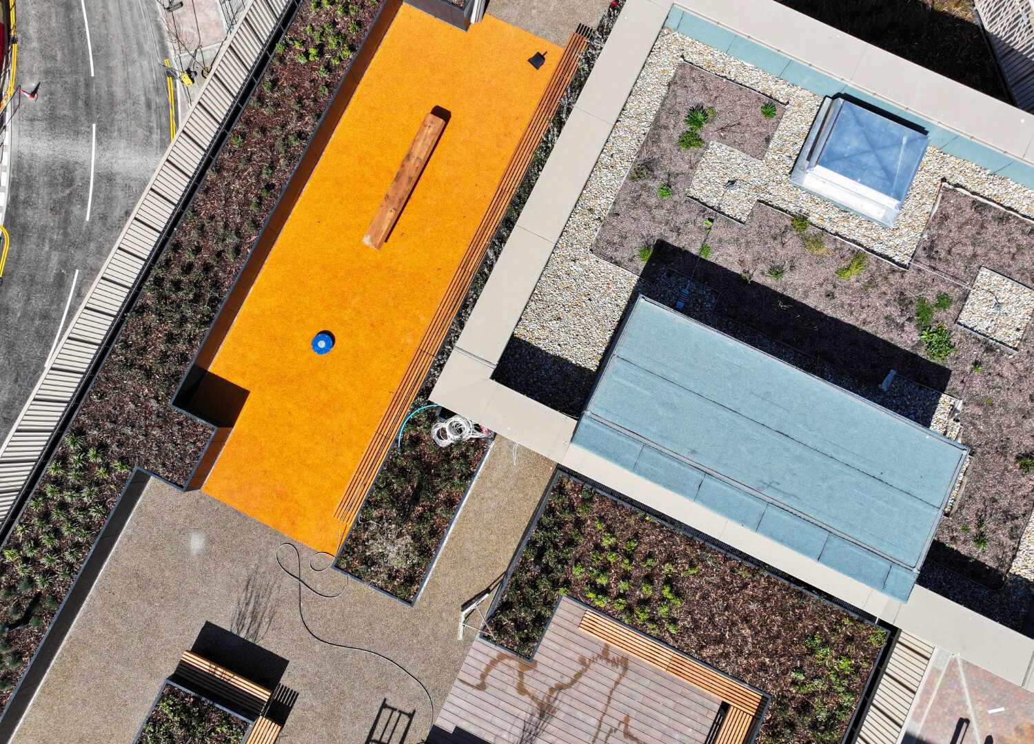 Aerial view of residential buildings with bright orange rectangular roof, blue swimming pool, and geometric arrangement of structures.