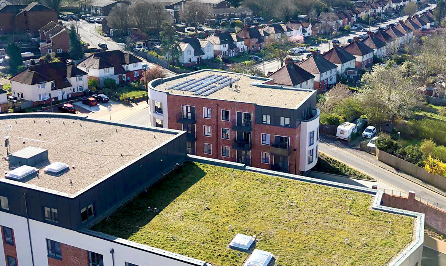 Aerial view of modern red brick apartment buildings with flat roofs, green courtyard, and surrounding residential neighbourhood.